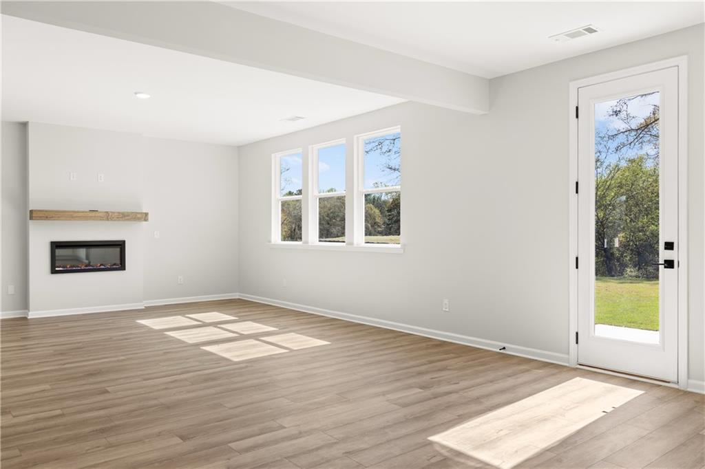 Bright living room featuring gas fireplace, hardwood floors, large windows, and sliding doors to green backyard in Davidson Homes The Hickory B, Winder, Georgia