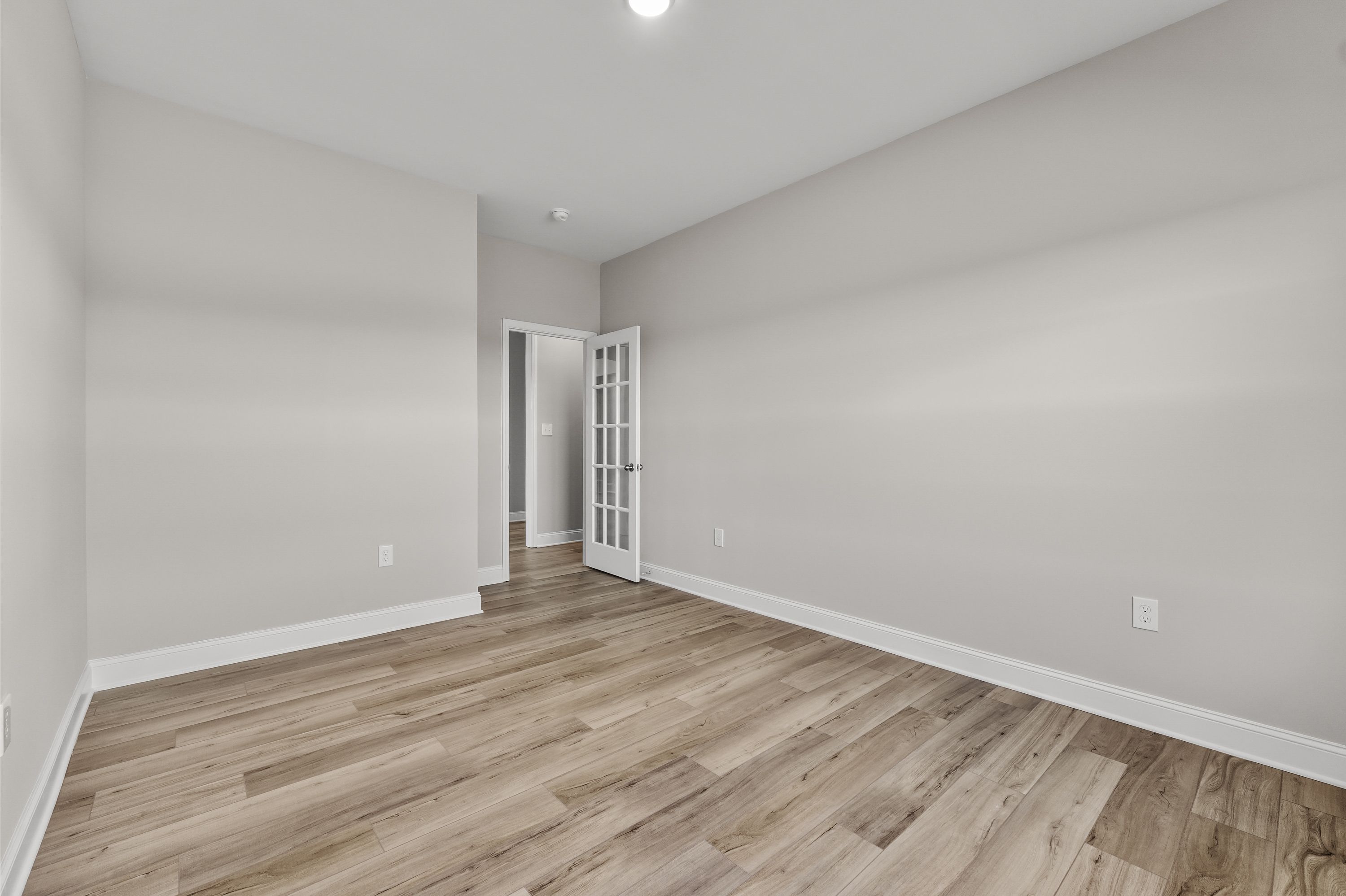 Spacious empty bedroom in The Valencia Davidson Homes design with light gray walls, hardwood floors, and French doors