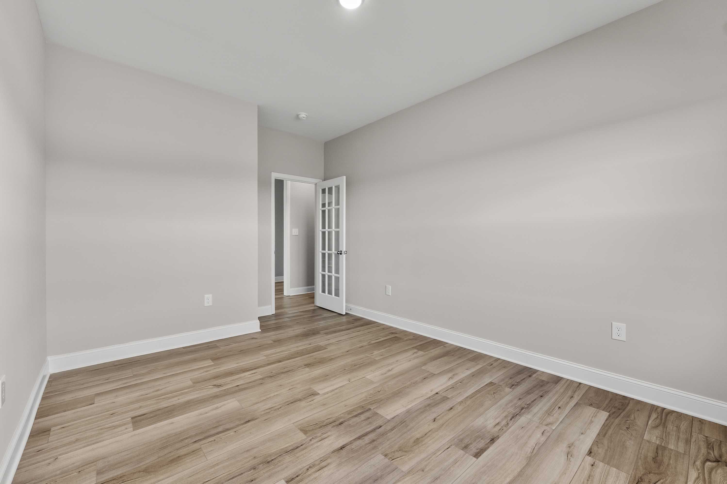 Spacious empty bedroom in The Valencia Davidson Homes design with light gray walls, hardwood floors, and French doors