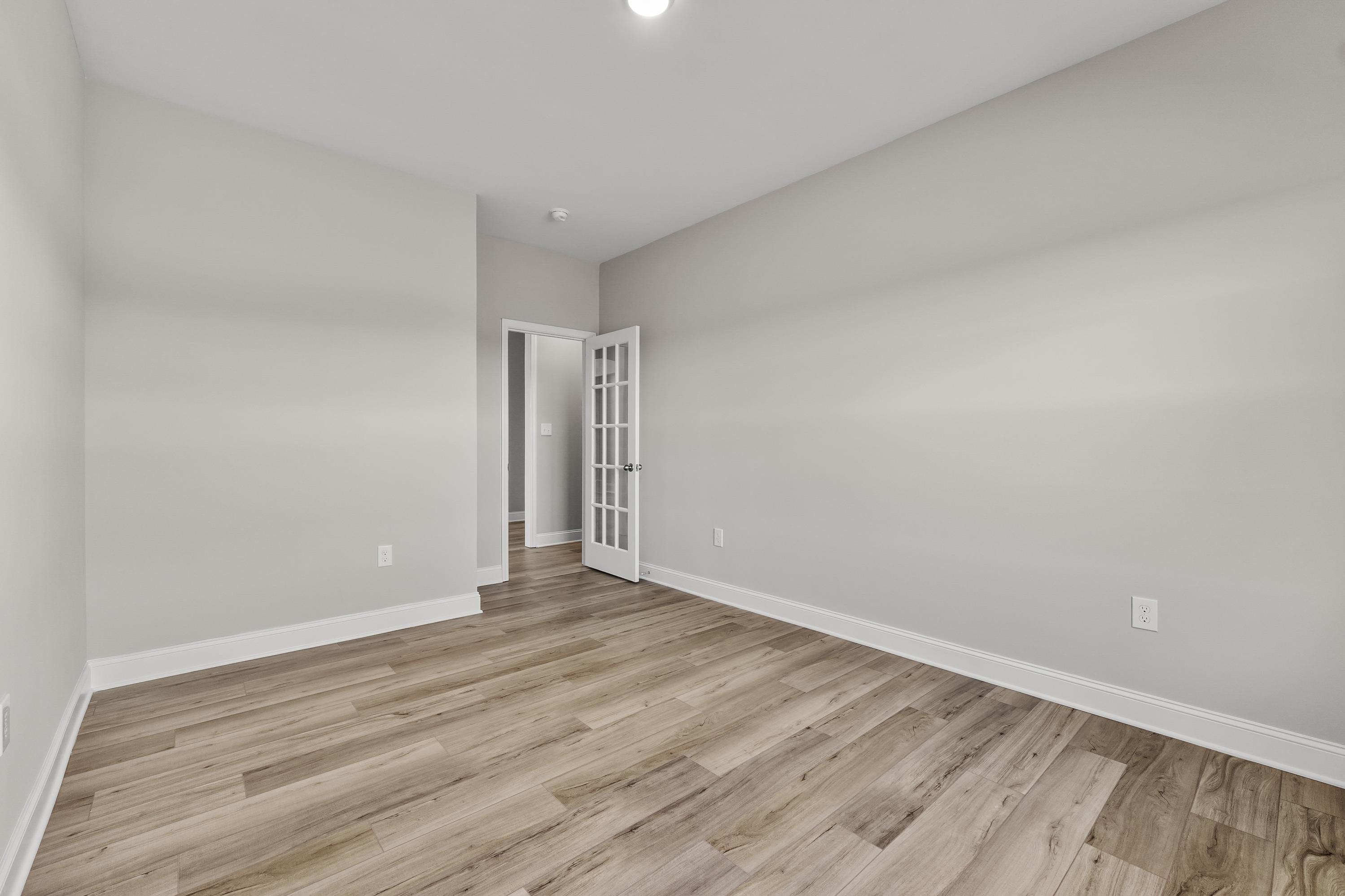 Spacious empty bedroom in The Valencia Davidson Homes design with light gray walls, hardwood floors, and French doors
