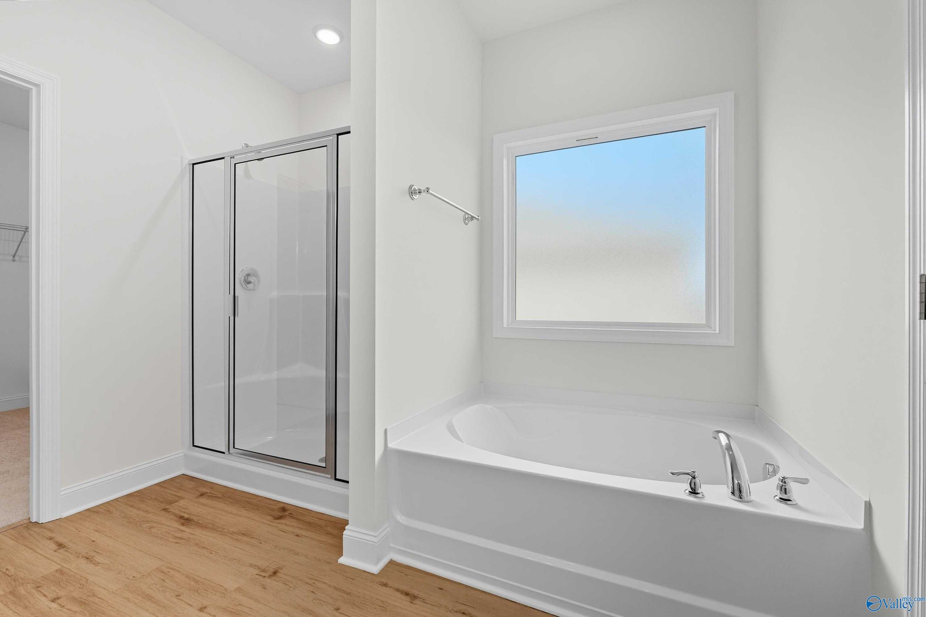 Modern master bathroom featuring glass shower, corner soaking tub, and frosted window in Davidson Homes The Everett, Meridianville, Alabama