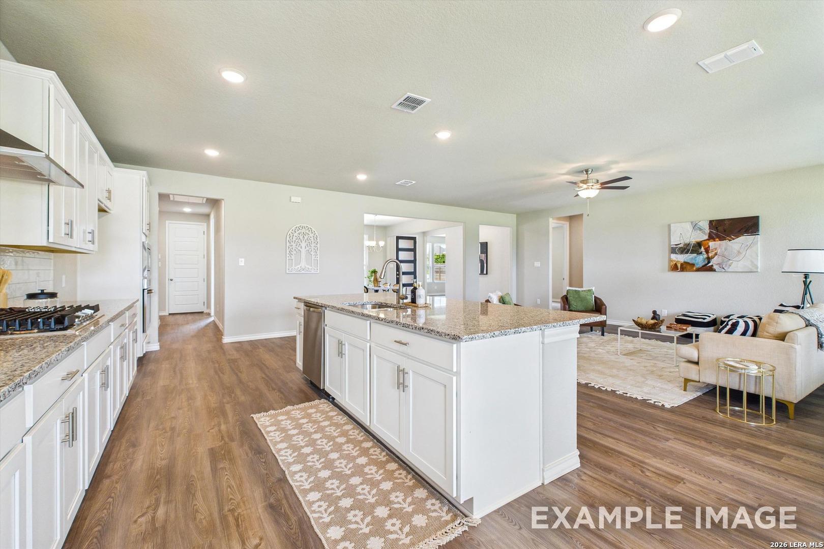 Open-concept kitchen with granite island and white cabinets in The Foster F floor plan by Davidson Homes in Castroville, TX.