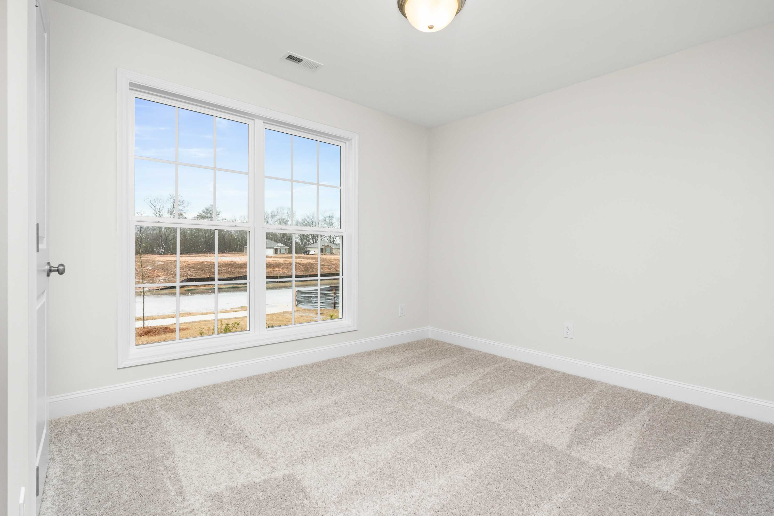 Bright secondary bedroom in The Asheville home design with beige carpet, white walls, and large window overlooking wooded view