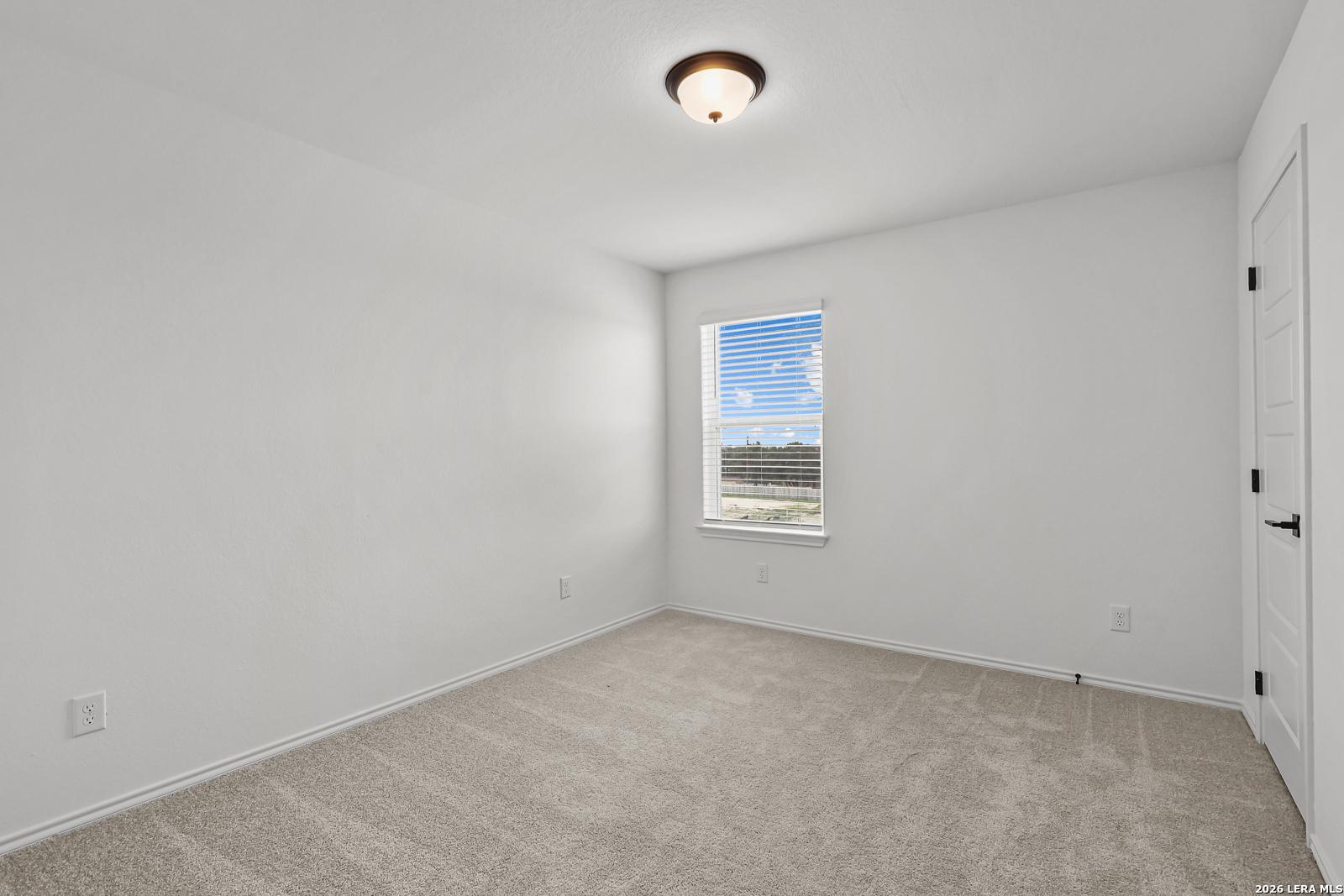 Bright, carpeted bedroom with white walls and a single window in The Gillian C floor plan at Meadows at Oak Creek, TX.
