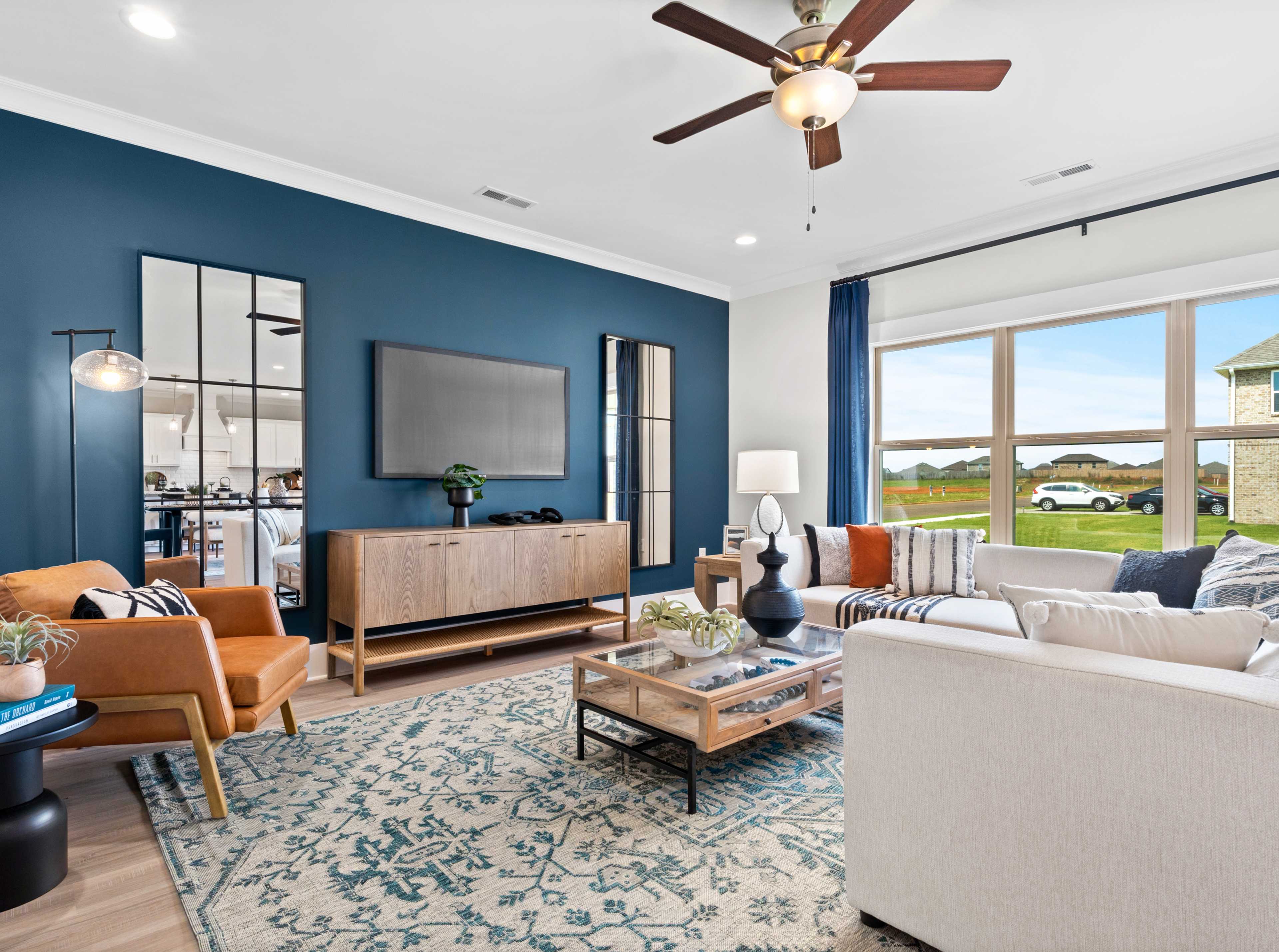 Cozy living room interior at Walker's Hill in Meridianville AL featuring navy walls, mirrored accents, mounted TV, orange armchair, white sofa, and large windows