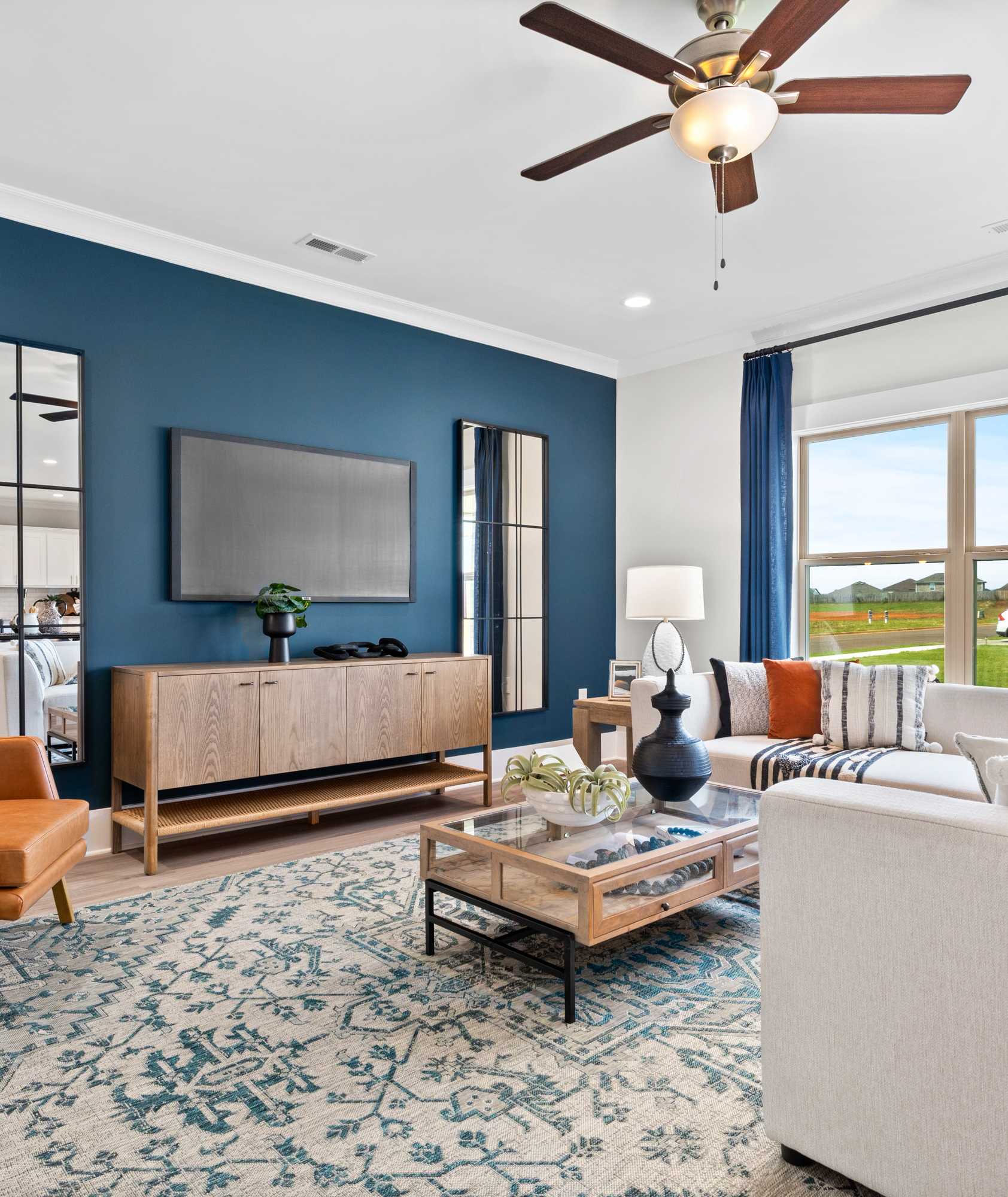 Cozy living room interior at Walker's Hill in Meridianville AL featuring navy walls, mirrored accents, mounted TV, orange armchair, white sofa, and large windows