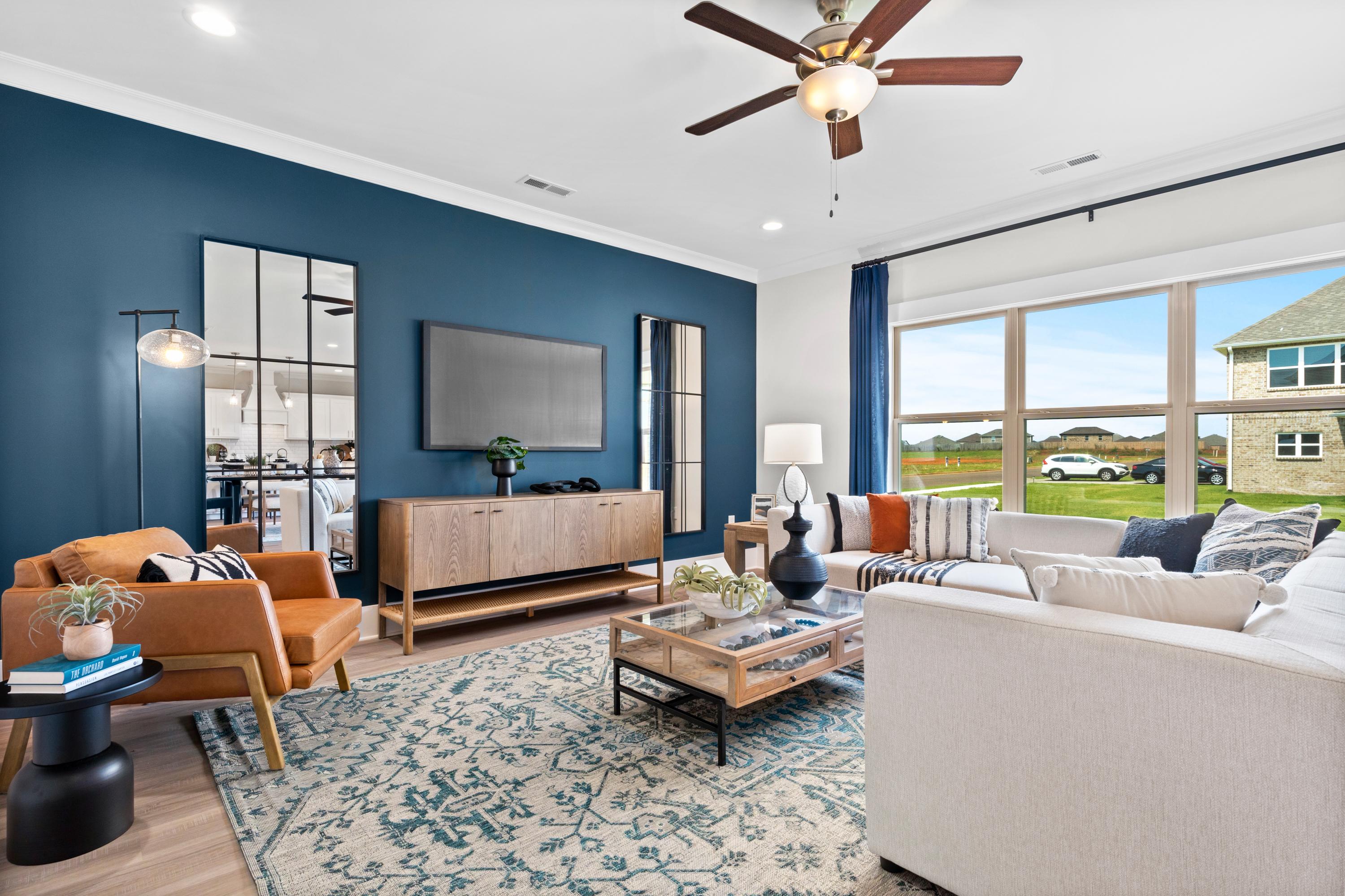 Spacious living room in The Chelsea A with navy walls, large windows, white sectional sofa, orange armchair, and modern credenza