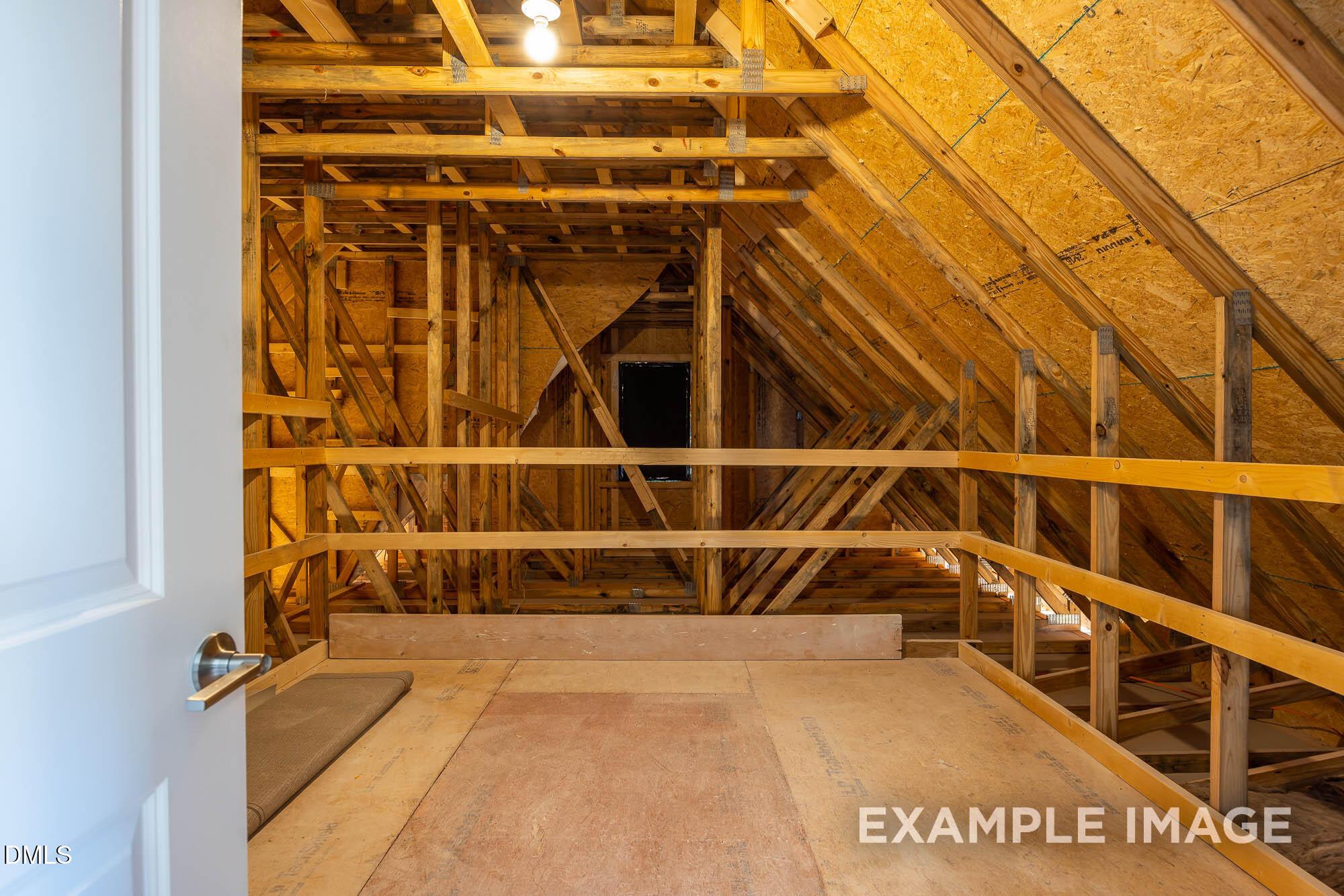 Unfinished attic bonus room with exposed wooden framing, yellow insulation, and railing in Davidson Homes The Cypress B II, Angier, NC