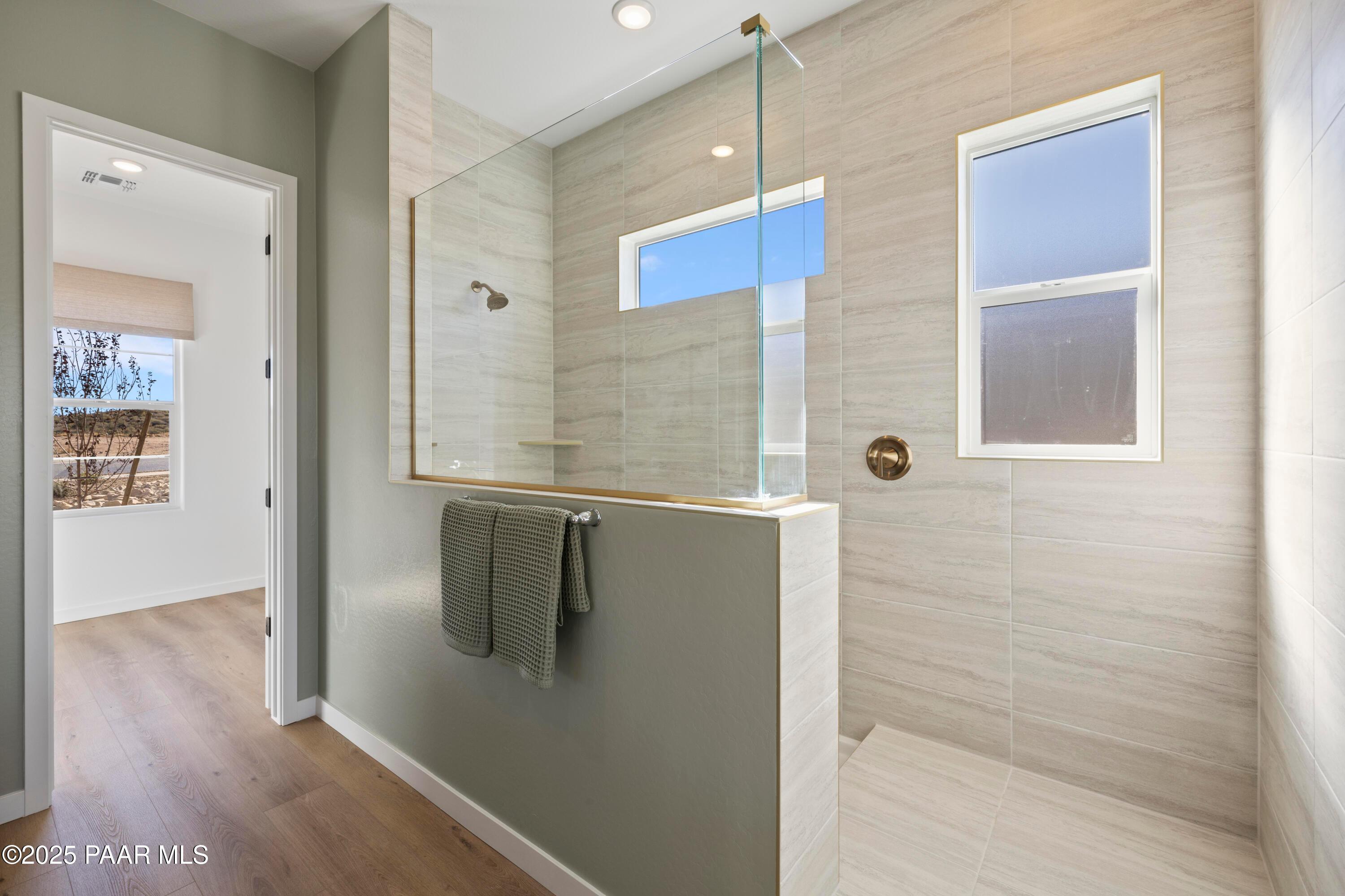 Frameless glass walk-in shower with beige tile surround and towels in master bath of Davidson Homes The Blaze D, Prescott, Arizona