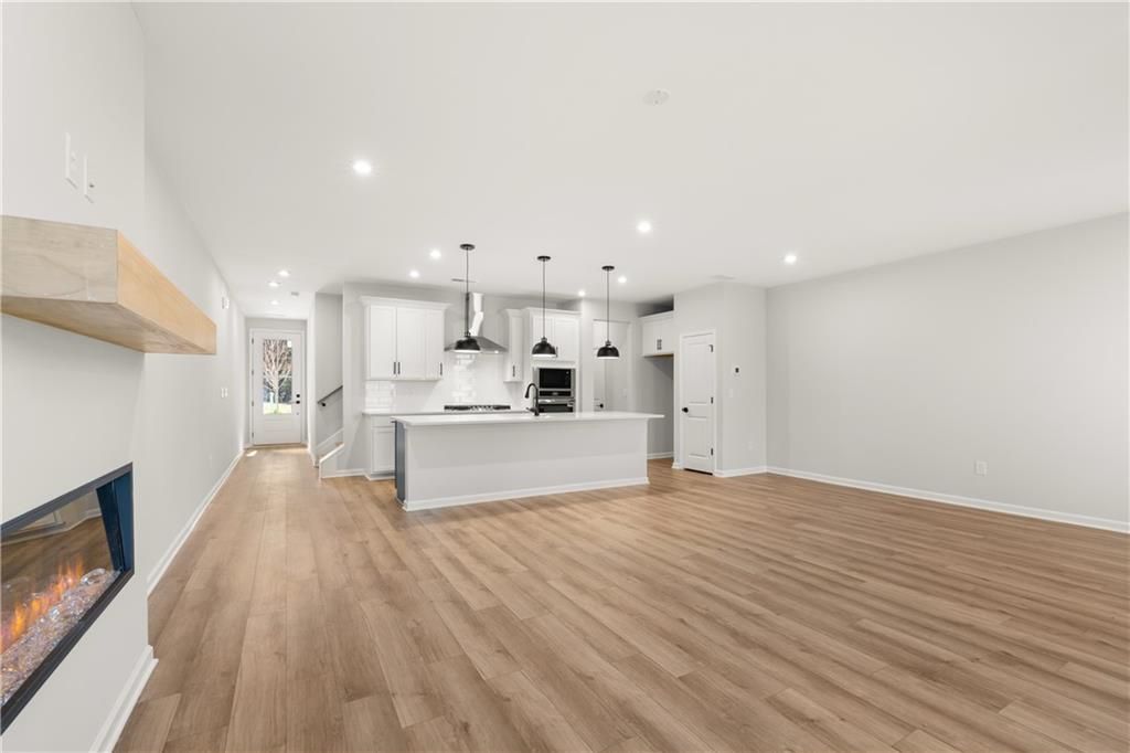 Open-concept living room with modern white kitchen island, gas fireplace, and hardwood floors in Davidson Homes The Cary A, Winder, GA