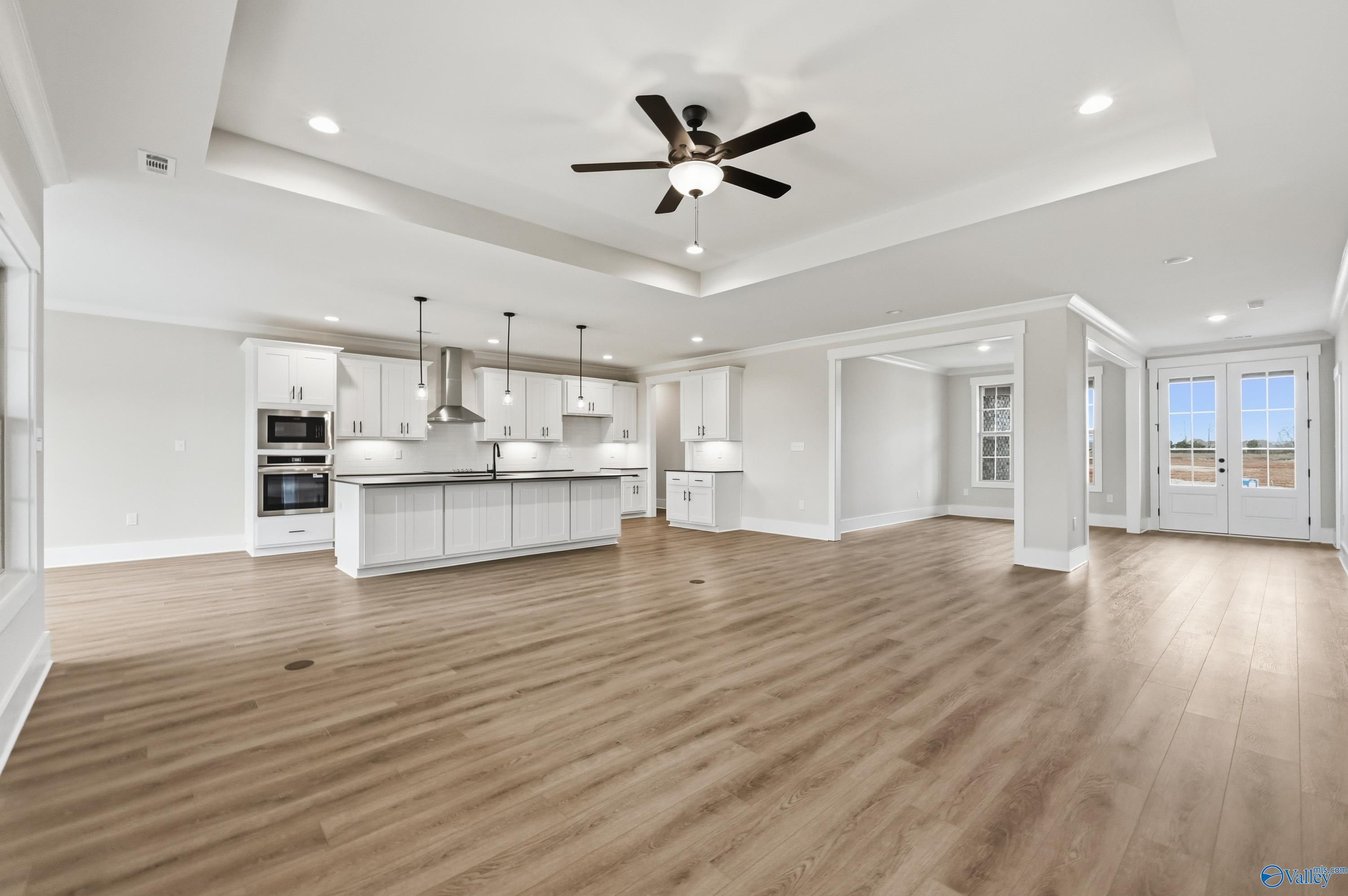 Open-concept kitchen-living area with white cabinets, island, pendant lights, and ceiling fan in The Finleigh home, Meridianville, Alabama