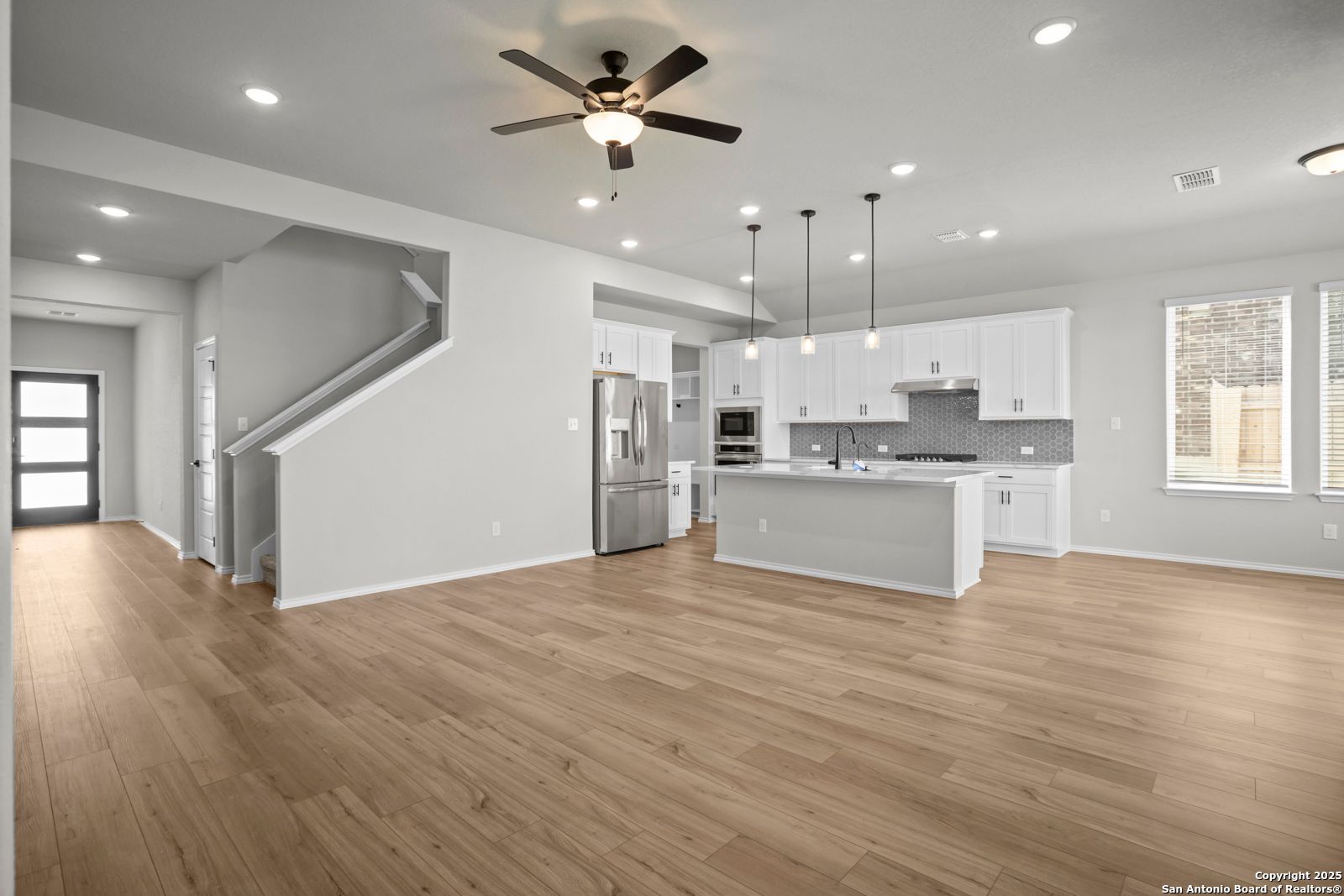 Open-concept kitchen and living area with white cabinets, stainless fridge, island, ceiling fan, and hardwood floors in Davidson Homes The Sequoia A, Converse, Texas