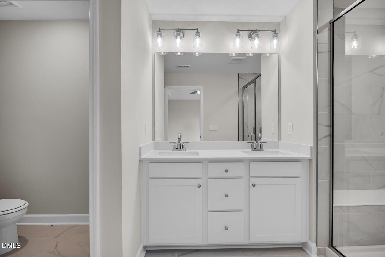 Modern double vanity with white cabinets, marble shower, and neutral tones in Davidson Homes The Avery, Knightdale, NC