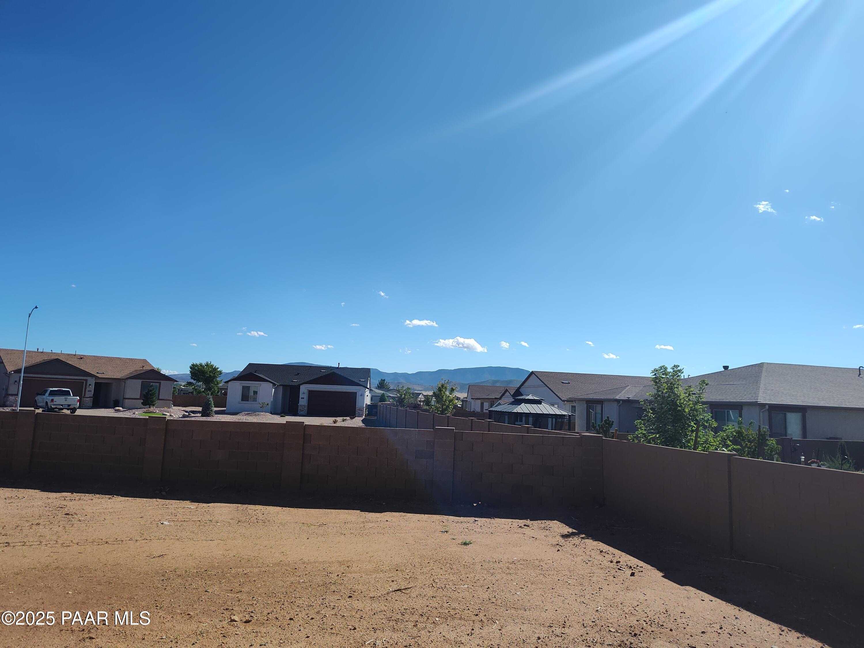Empty lot surrounded by modern single-story homes in North Ridge at Pronghorn Ranch, Prescott Valley, Arizona, with distant mountains and sunny blue sky