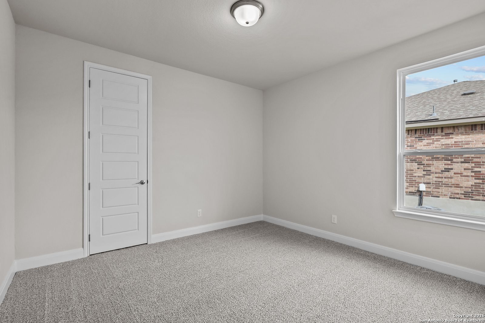 Empty bedroom with light gray walls, neutral carpet, white door, and window view in Davidson Homes The Lanier H, Ladera, San Antonio