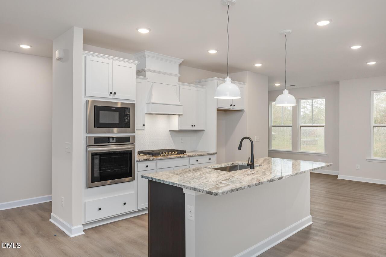 Elegant kitchen with white shaker cabinets, stainless double oven, veined quartz island, and pendant lights in Davidson Homes The Mitchell plan, Knightdale NC