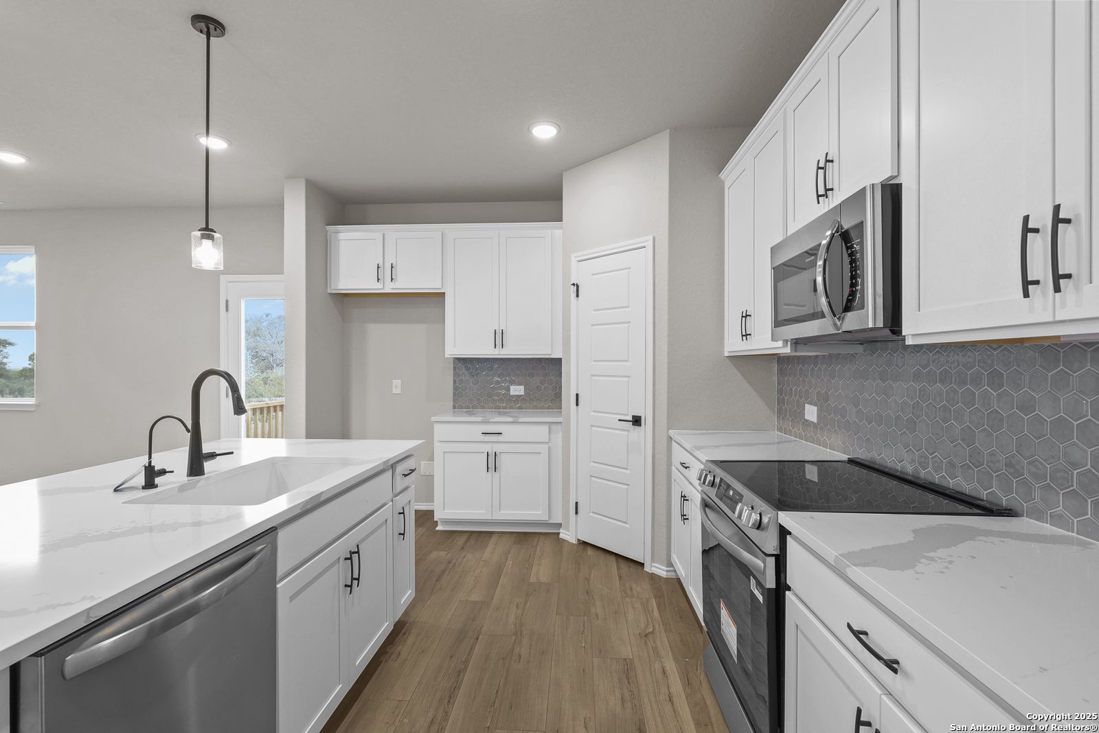 Modern kitchen with white shaker cabinets, stainless appliances, gray quartz island, hexagon tile backsplash in Davidson Homes The Murray J, San Antonio