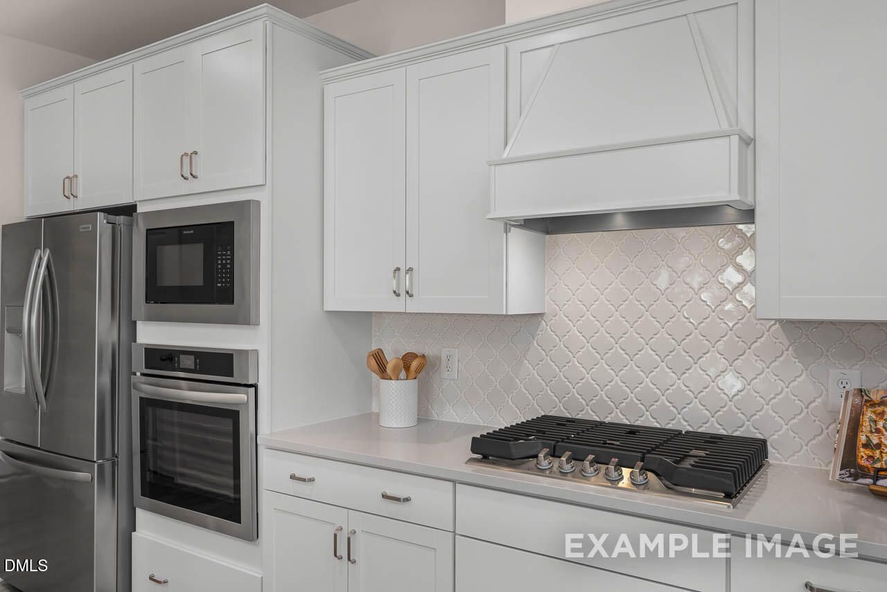 Modern white kitchen featuring stainless steel appliances, gas cooktop, and subway tile backsplash in Davidson Homes The Hickory II C, Wake Forest, NC