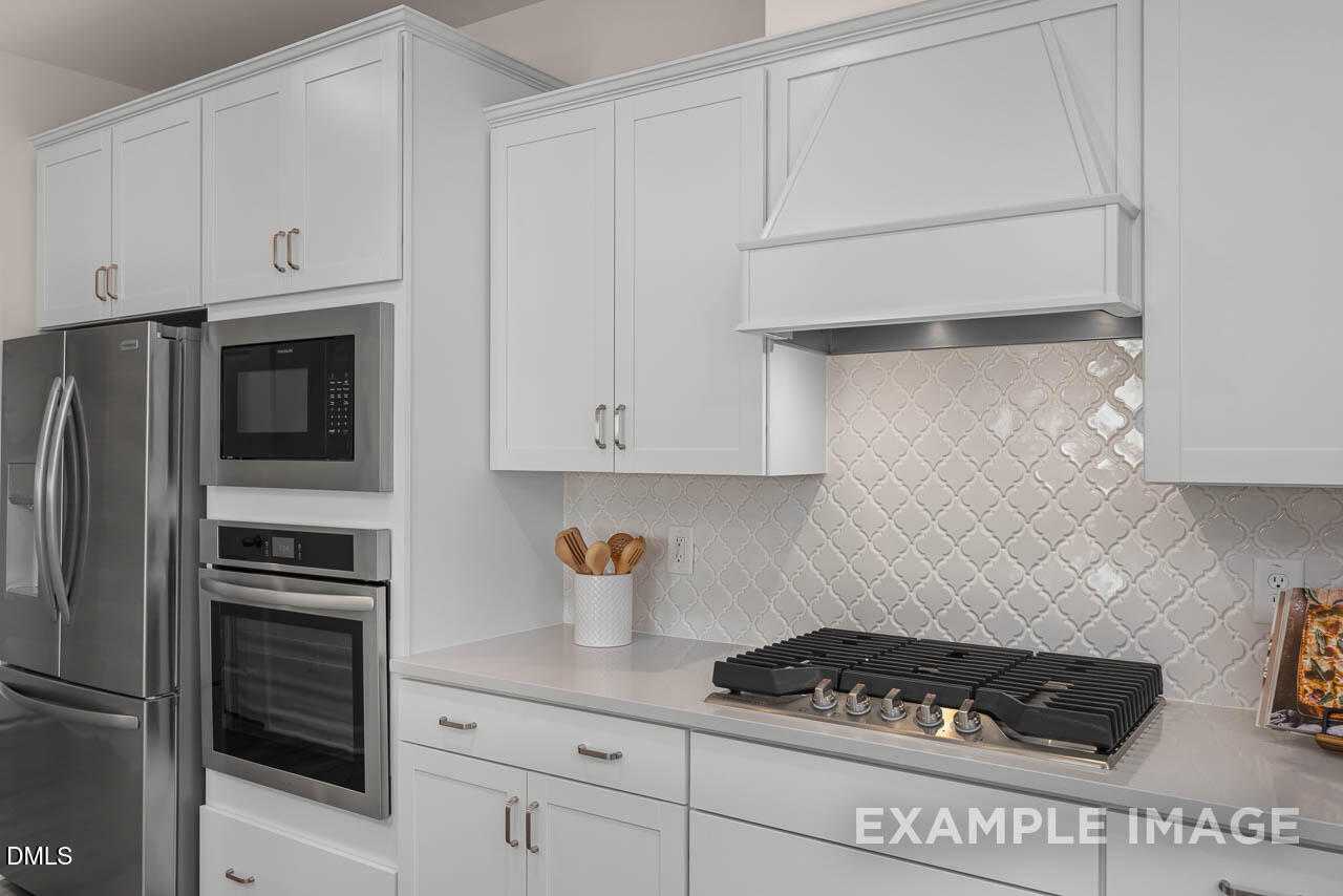 Modern white kitchen featuring stainless steel appliances, gas cooktop, and subway tile backsplash in Davidson Homes The Hickory II C, Wake Forest, NC