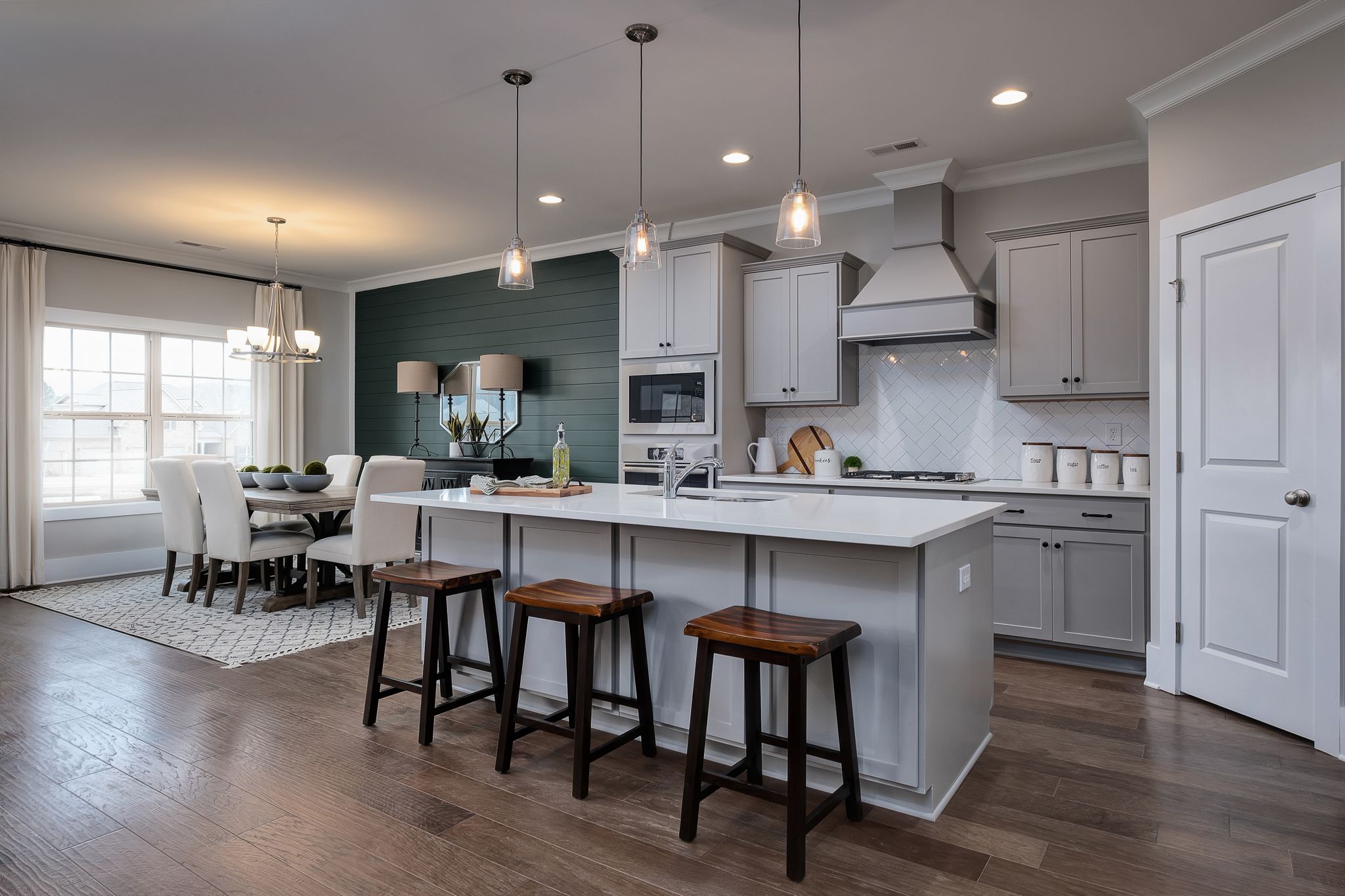 Modern kitchen with gray cabinets, subway tile backsplash, island bar stools, and adjacent dining area in Chimney Creek, Hampton Cove Alabama