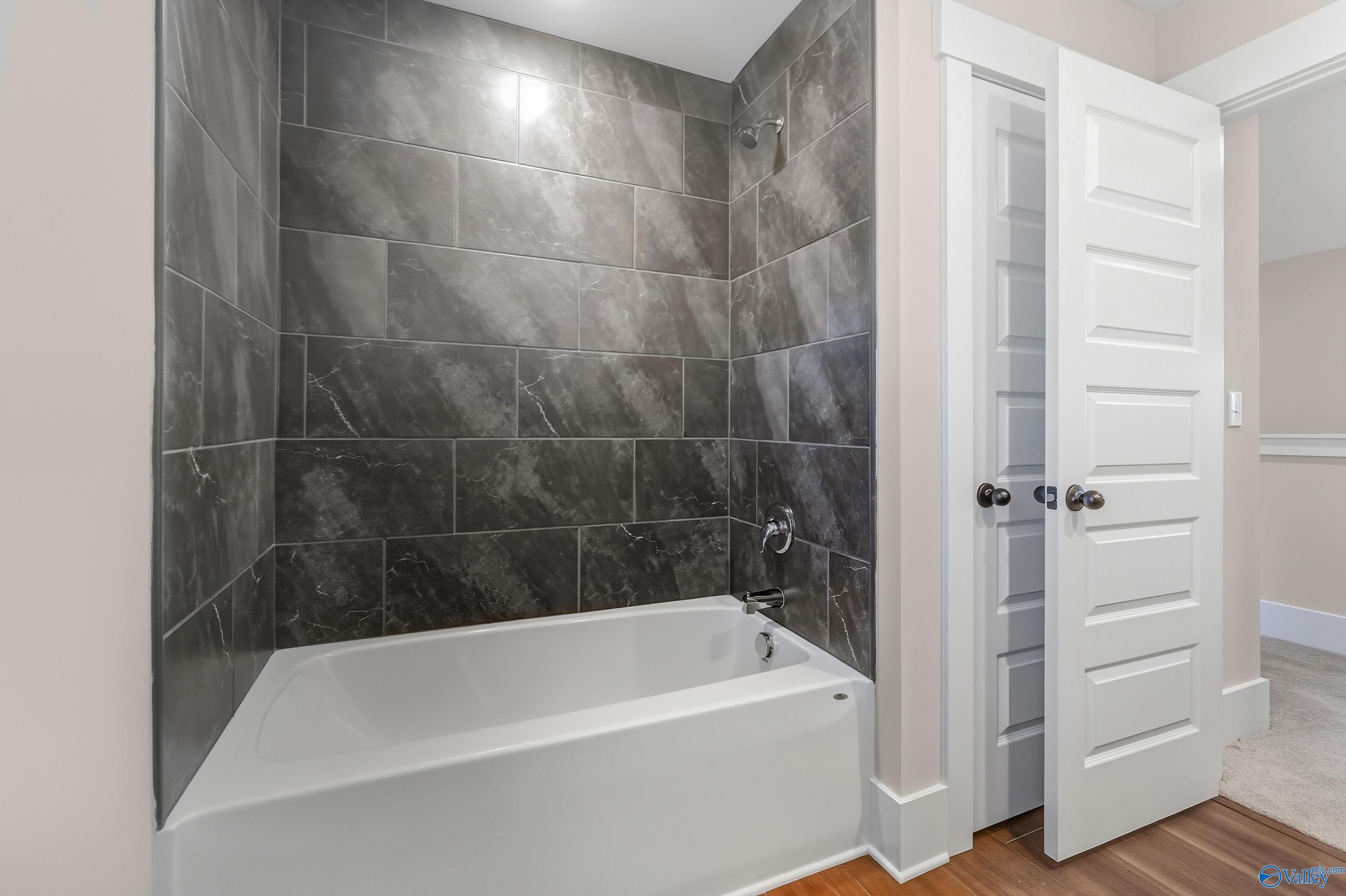 Elegant bathroom with slate gray tile shower, white soaking tub, and double doors in Davidson Homes The Shelby A, Athens, Alabama