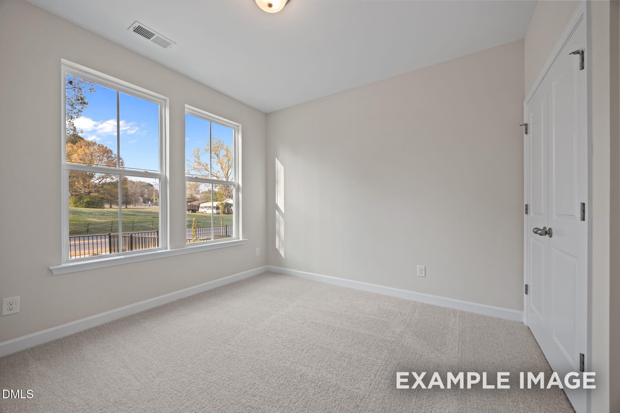 Bright empty bedroom featuring large windows with autumn tree views, beige walls, and carpet in Davidson Homes The Avery, Knightdale, NC