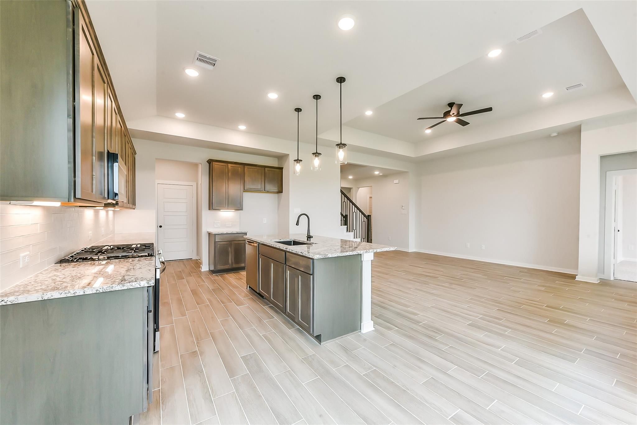 Modern open-concept kitchen featuring gray shaker cabinets, quartz countertops, stainless appliances, and island in Davidson Homes The Sequoia C, Crosby, Texas