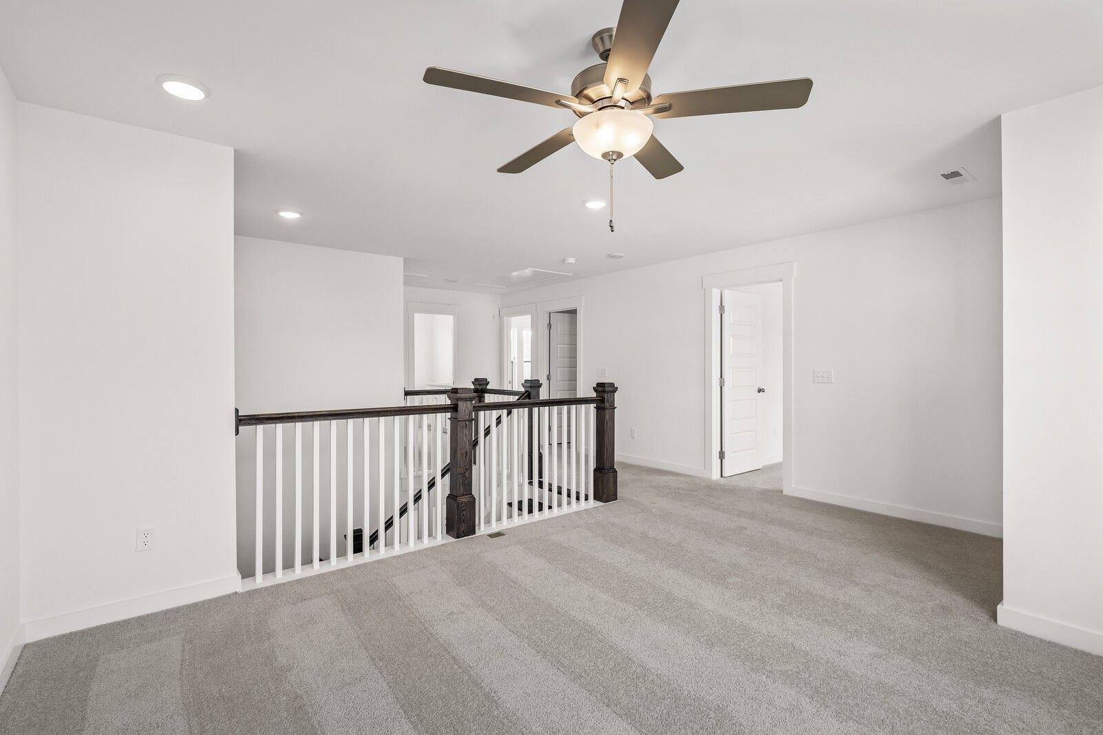 Bright upstairs hallway with dark wood railing, neutral carpet, and ceiling fan in The Willow D home, Mt. Juliet, Tennessee