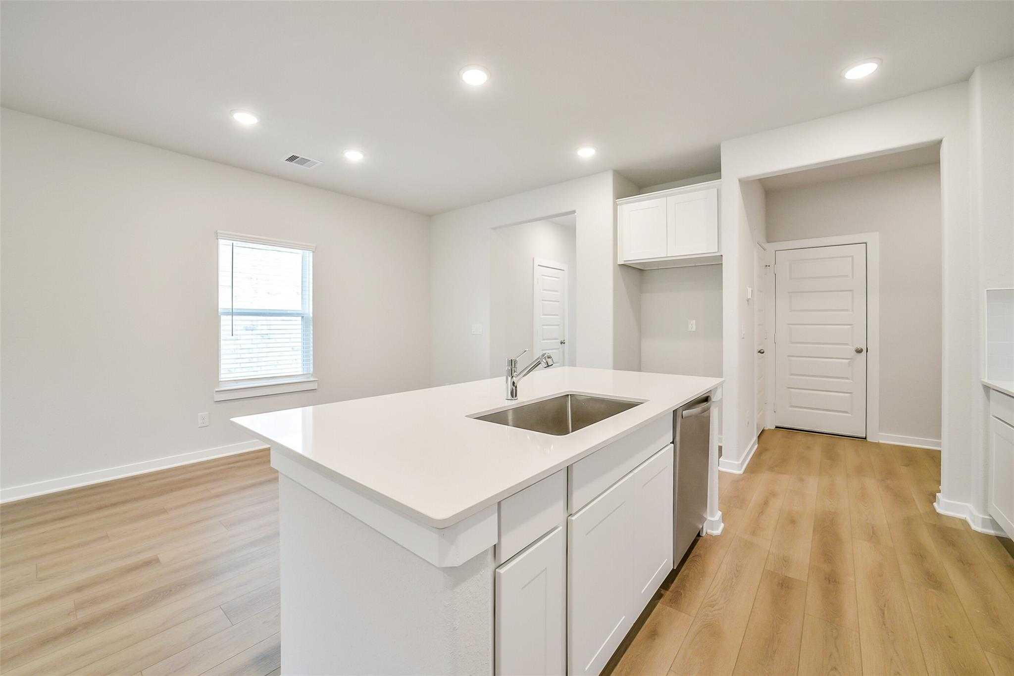 Modern white kitchen island with sink, dishwasher, and cabinets in Davidson Homes The Blanco E, Magnolia, Texas