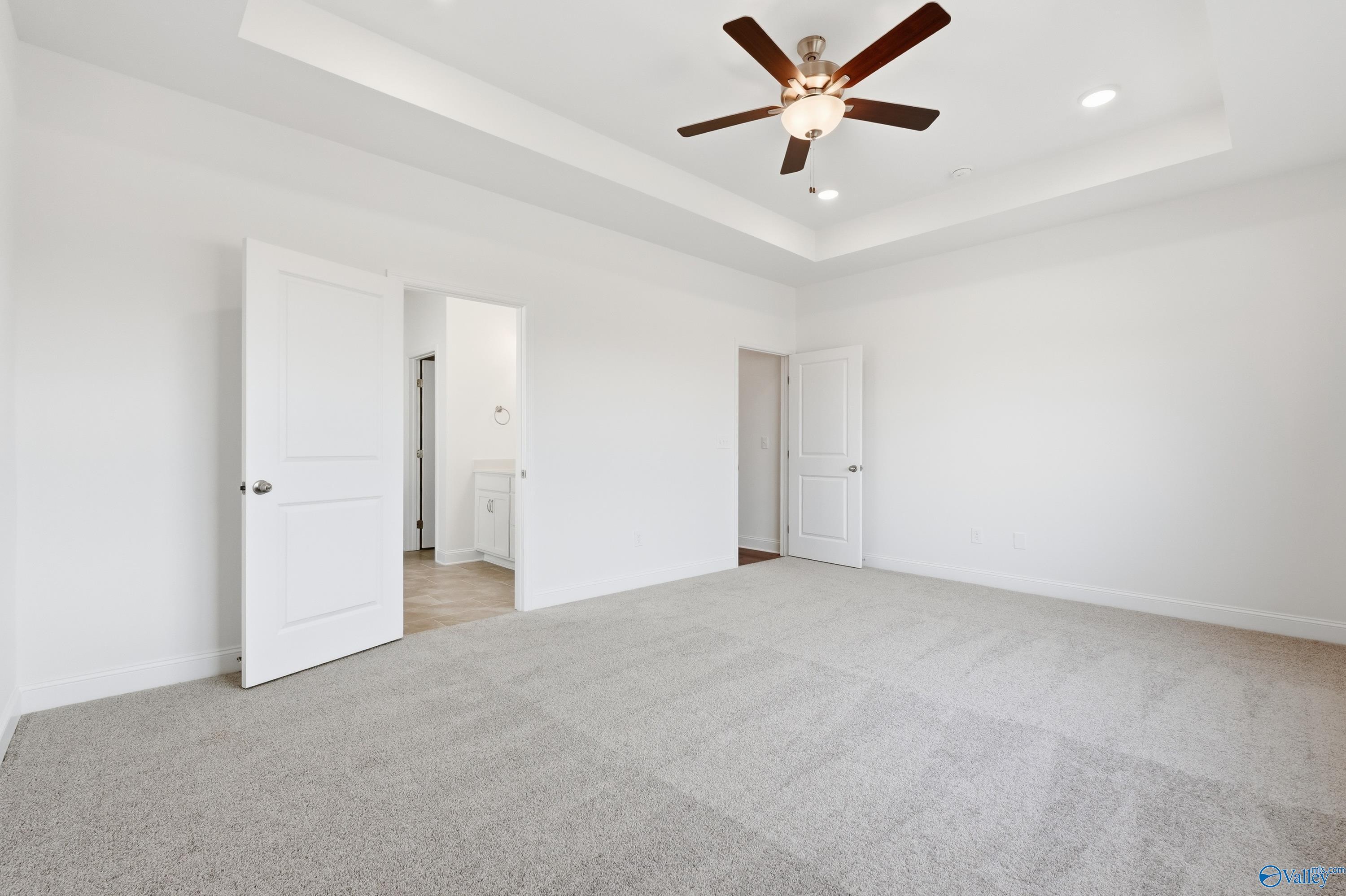 Spacious master bedroom with tray ceiling, ceiling fan, and en-suite bath access in Davidson Homes The Montgomery C, Harvest, AL