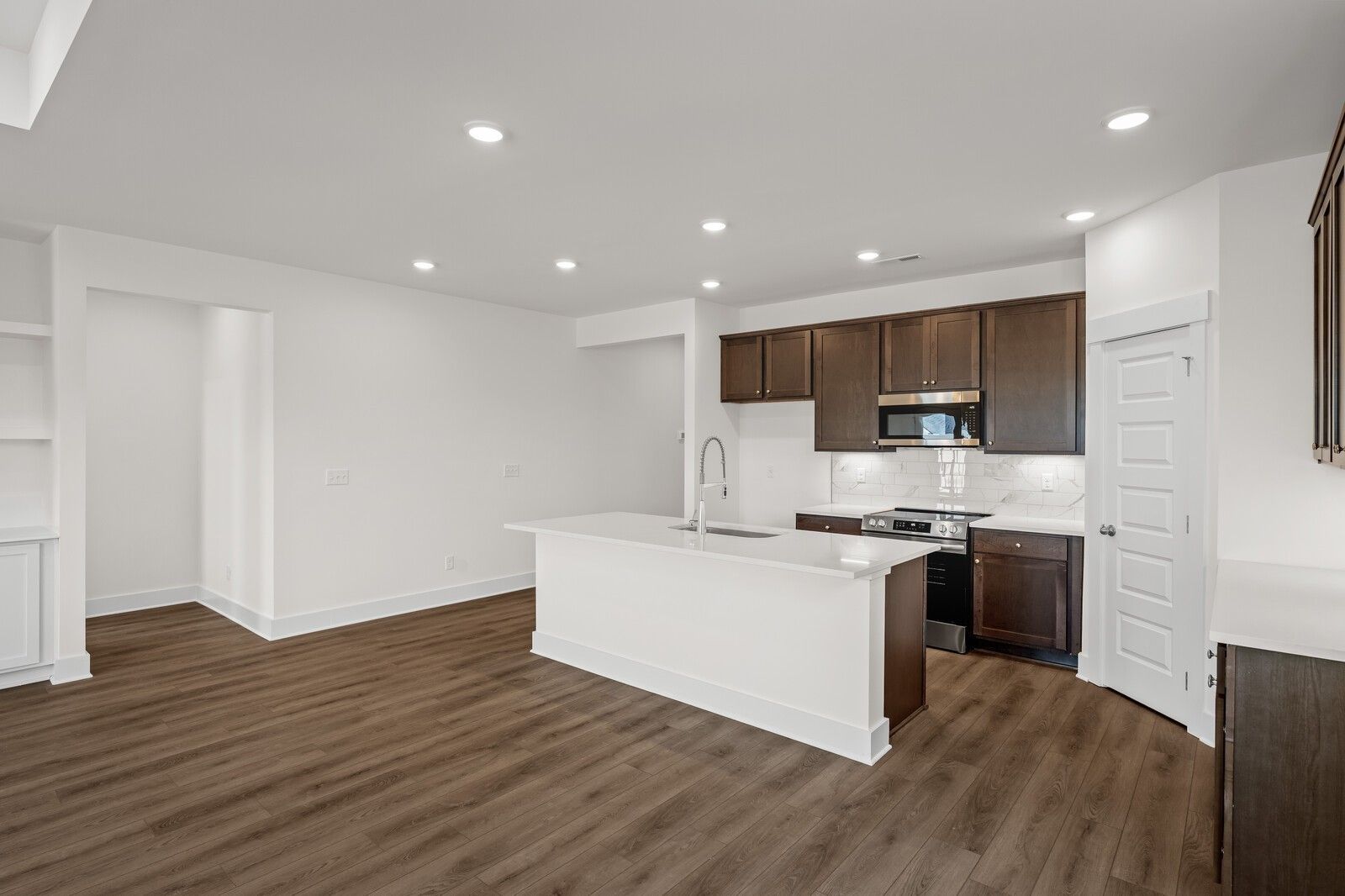 Open-concept kitchen with white island, dark wood cabinets, and luxury vinyl plank flooring in Davidson Homes Cottonwood E, Gallatin TN