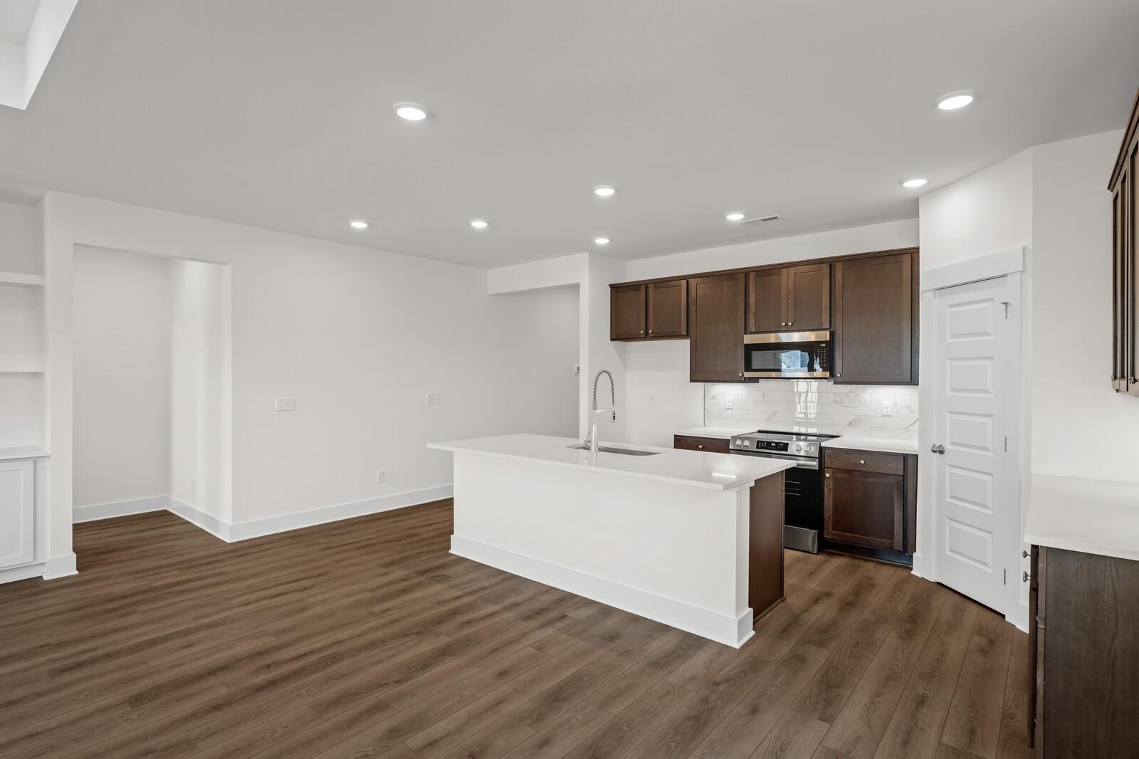 Open-concept kitchen with white island, dark wood cabinets, and luxury vinyl plank flooring in Davidson Homes Cottonwood E, Gallatin TN