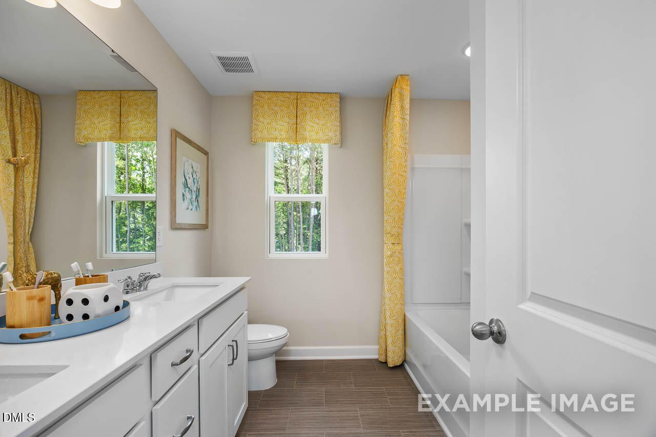 Elegant guest bathroom with white vanity, yellow curtains, garden view window, and tub in Davidson Homes The Willow B, Wake Forest NC