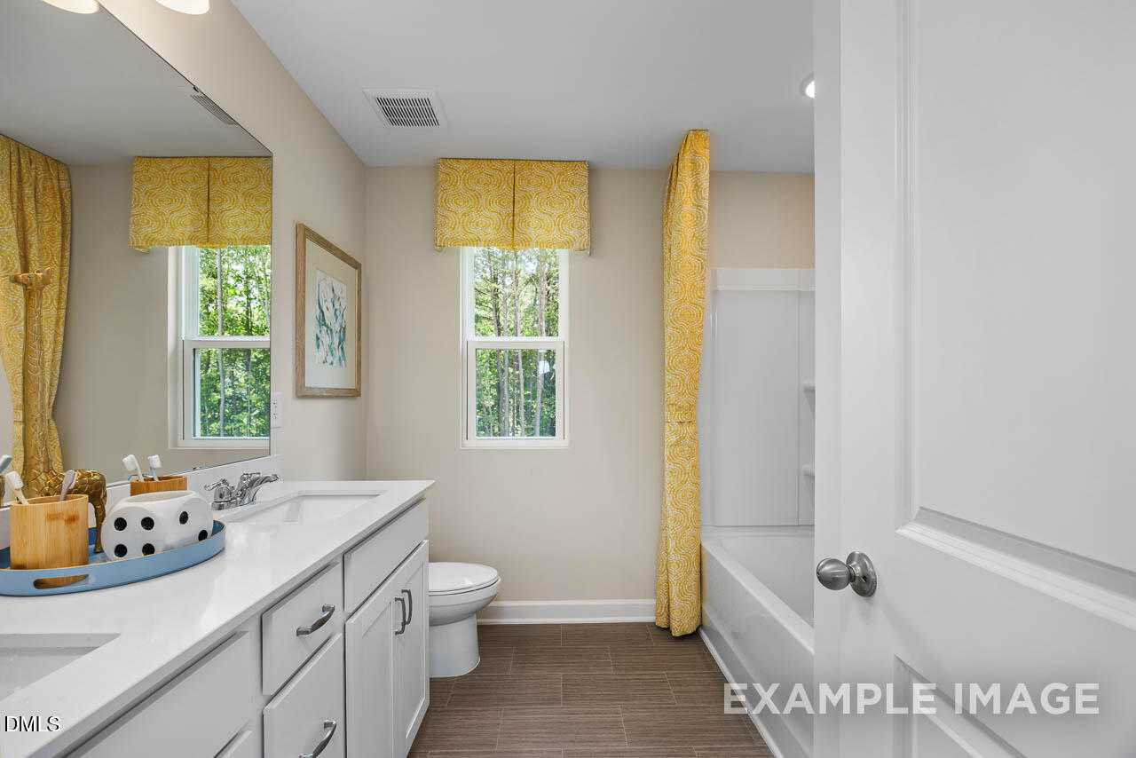 Bright guest bathroom with double vanity, soaking tub, yellow curtains, and tree views in Davidson Homes The Willow B, Lillington NC