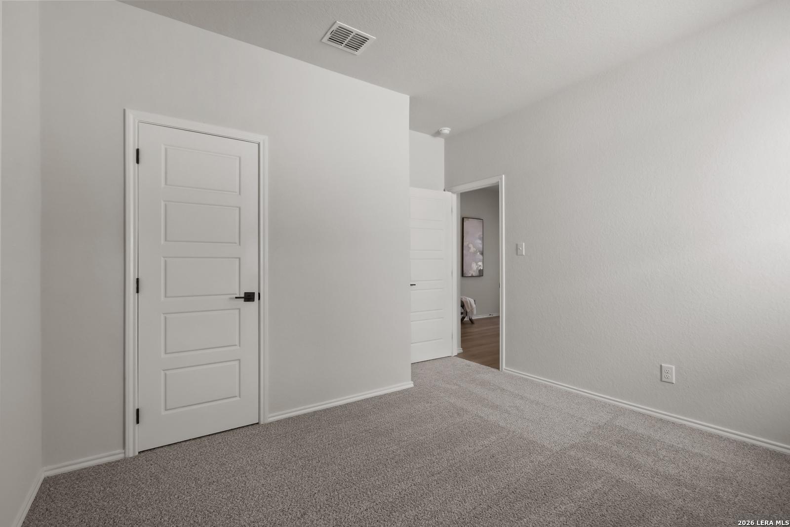 Bright empty secondary bedroom with white walls, carpet floor, and en-suite door in Davidson Homes The Daphne H, Seguin, Texas