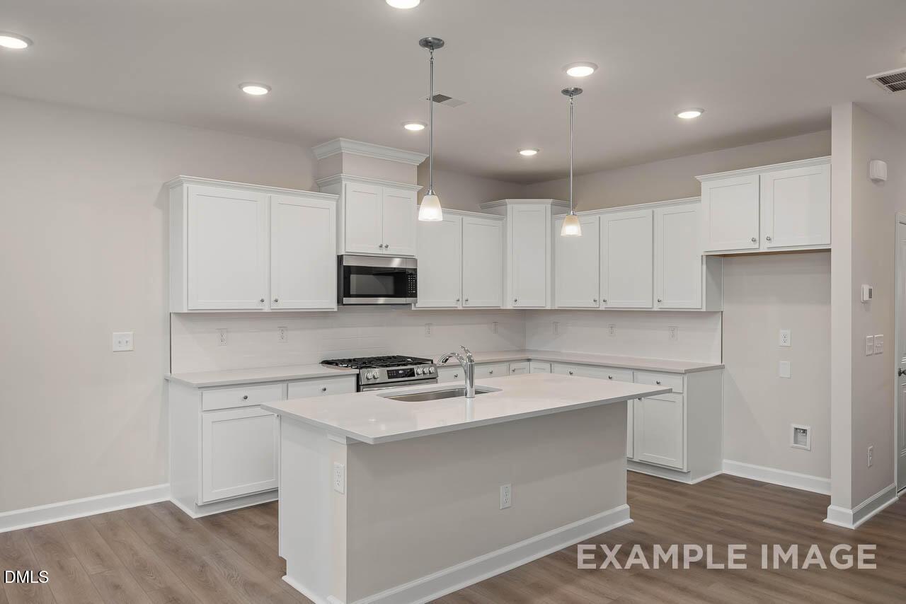 Modern white kitchen with quartz countertops, stainless steel appliances, and island in Davidson Homes The Graham, Fuquay-Varina