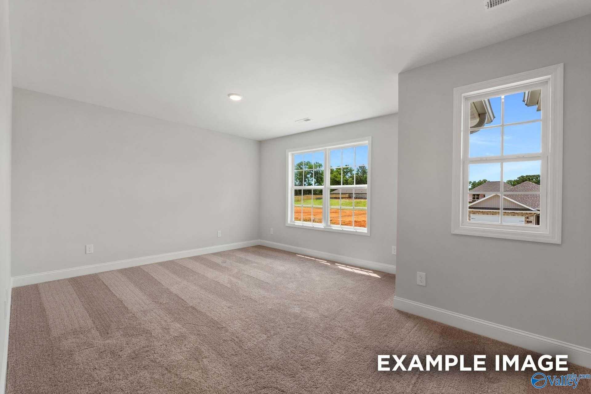 Spacious empty bedroom with neutral gray walls, beige carpet, and large windows showing wooded view in The Shelby C home, Meridianville, Alabama