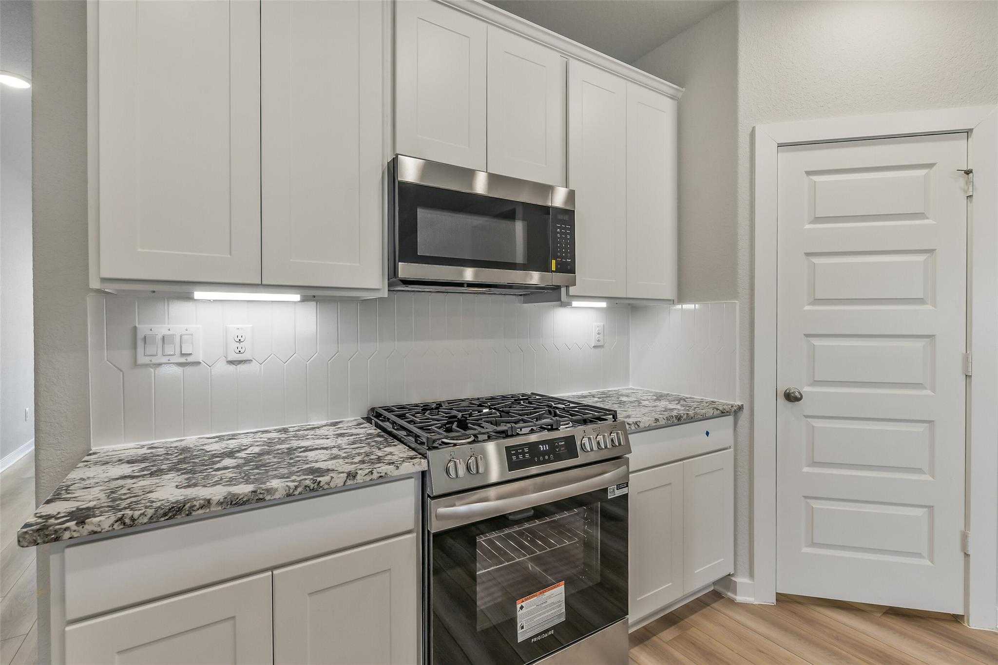 Contemporary kitchen with white shaker cabinets, speckled granite countertops, stainless steel gas range in Davidson Homes Rio Grande H, Magnolia TX