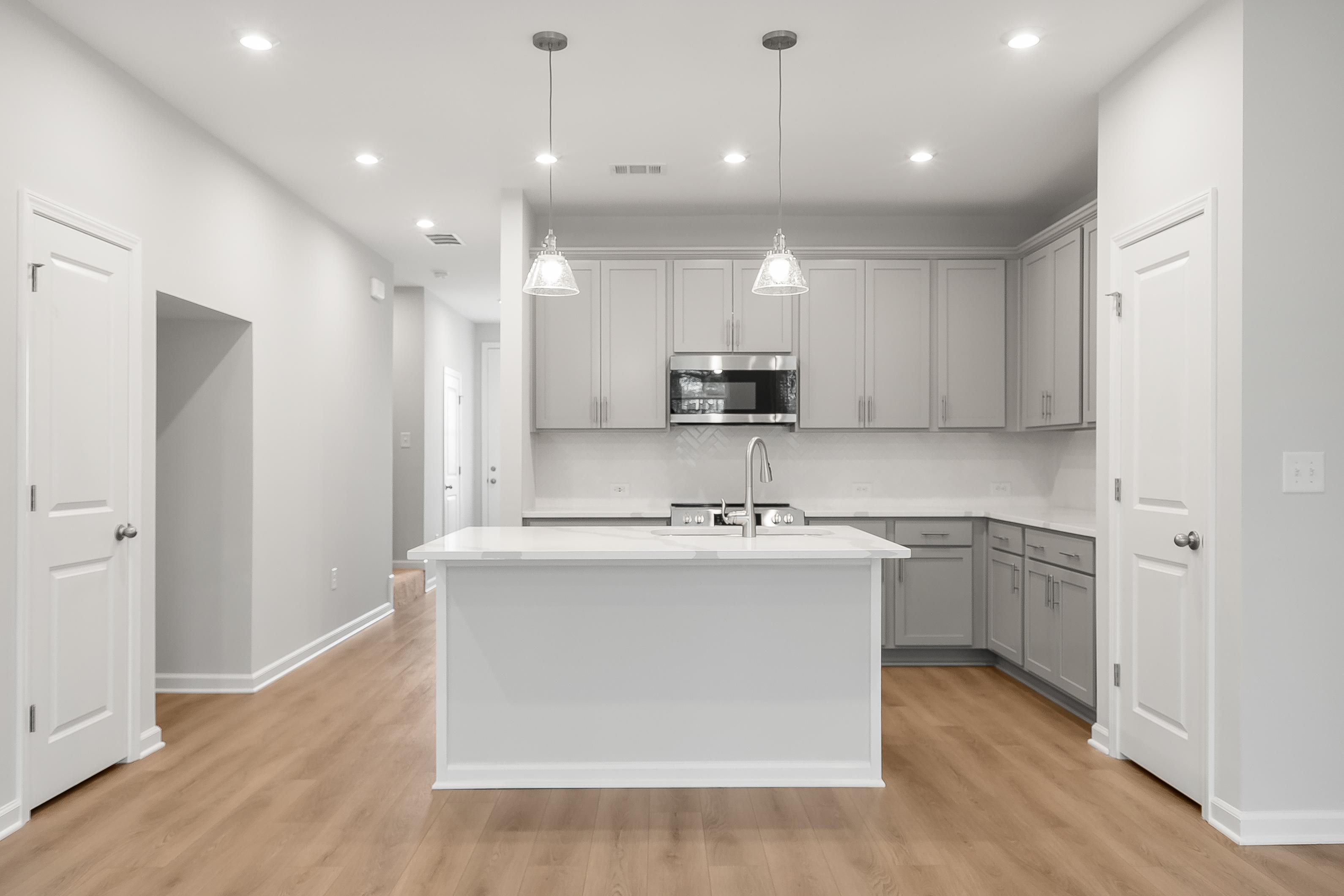 Spacious kitchen in The Durant A featuring white island with sink, gray shaker cabinets, stainless appliances, hardwood floors
