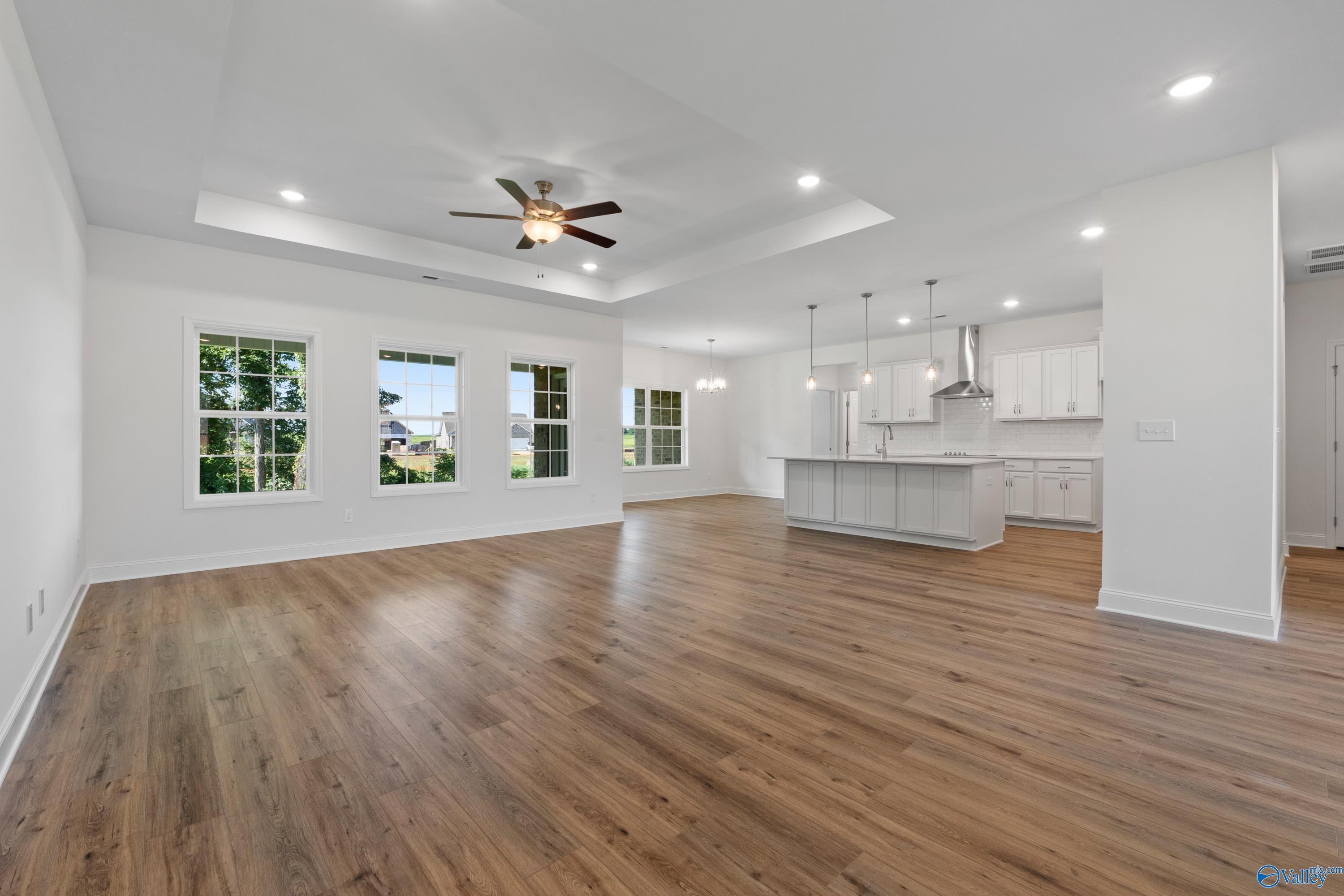 Open-concept kitchen-living area with white cabinets, island, hardwood floors, and large windows in The Oxford by Davidson Homes, Harvest, AL