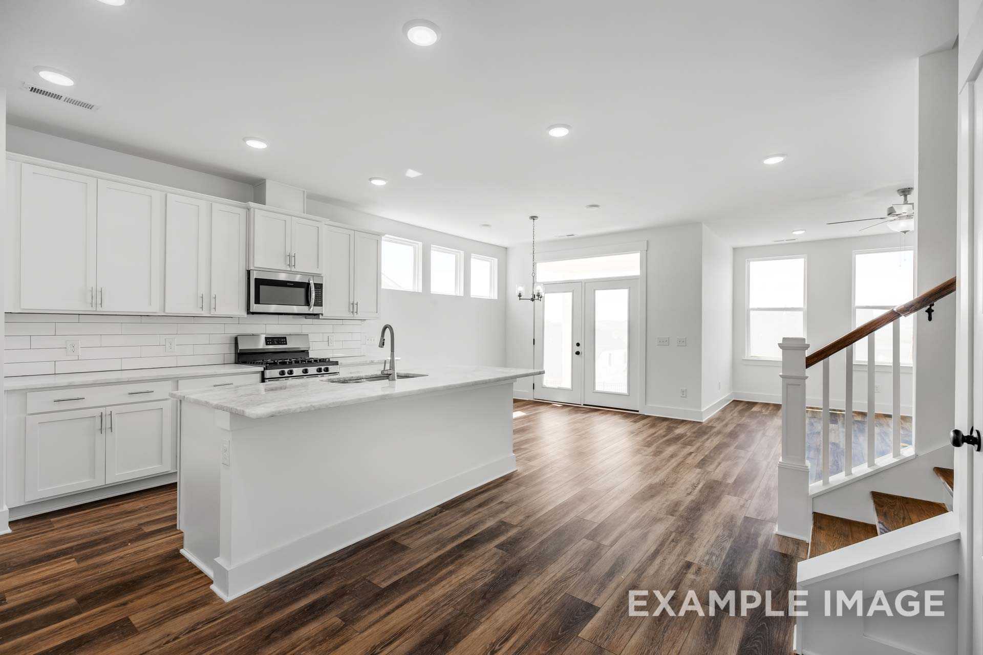 Modern open-concept kitchen in The Ash C featuring white shaker cabinets, large island, stainless appliances, and hardwood floors