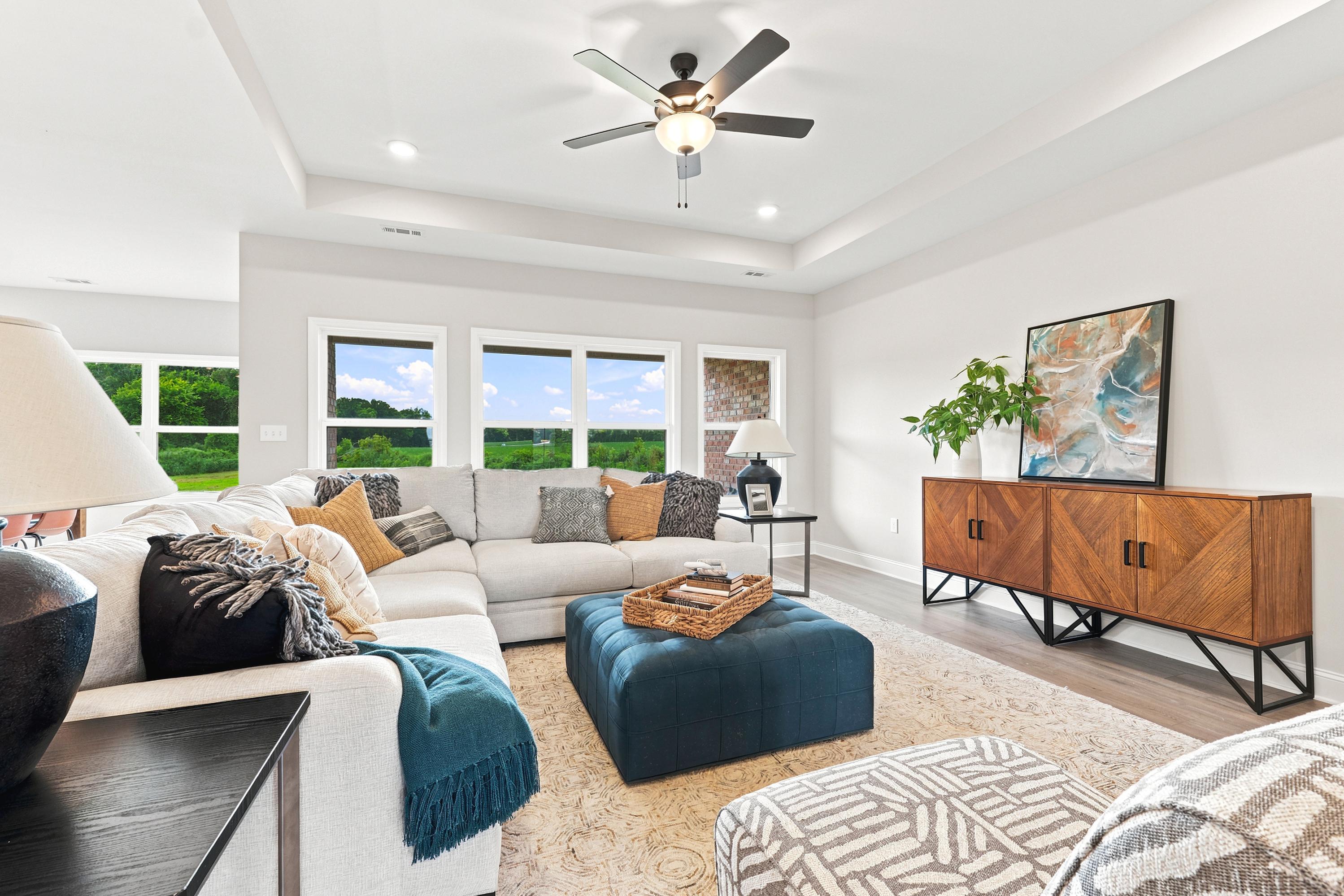Bright living room at Riverton Preserve in Huntsville, AL featuring a sectional sofa, blue ottoman, and modern decor.