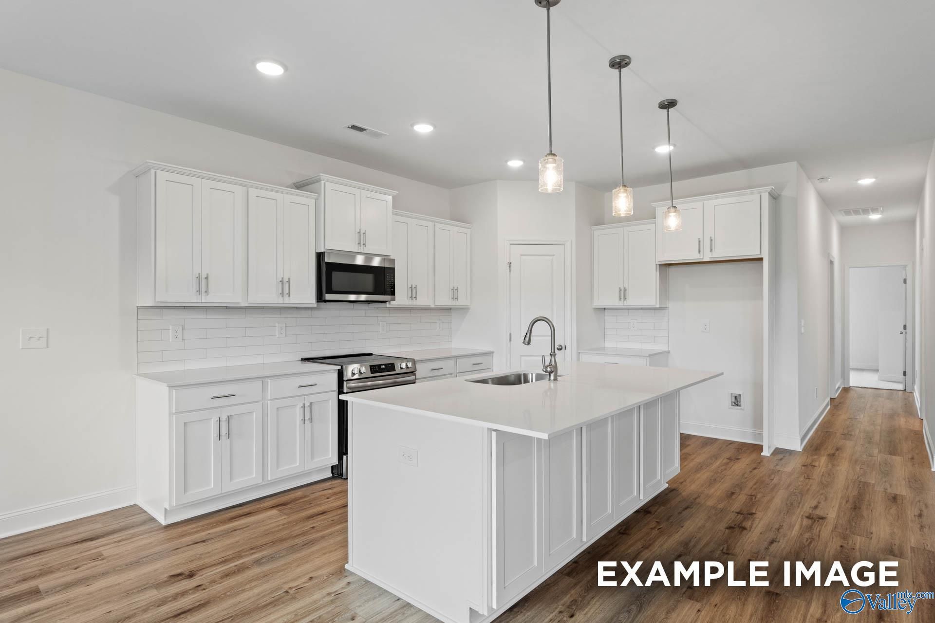 Modern kitchen with white cabinets, quartz island, and pendant lighting in The Rockford B plan at Kendall Downs, Toney, AL.