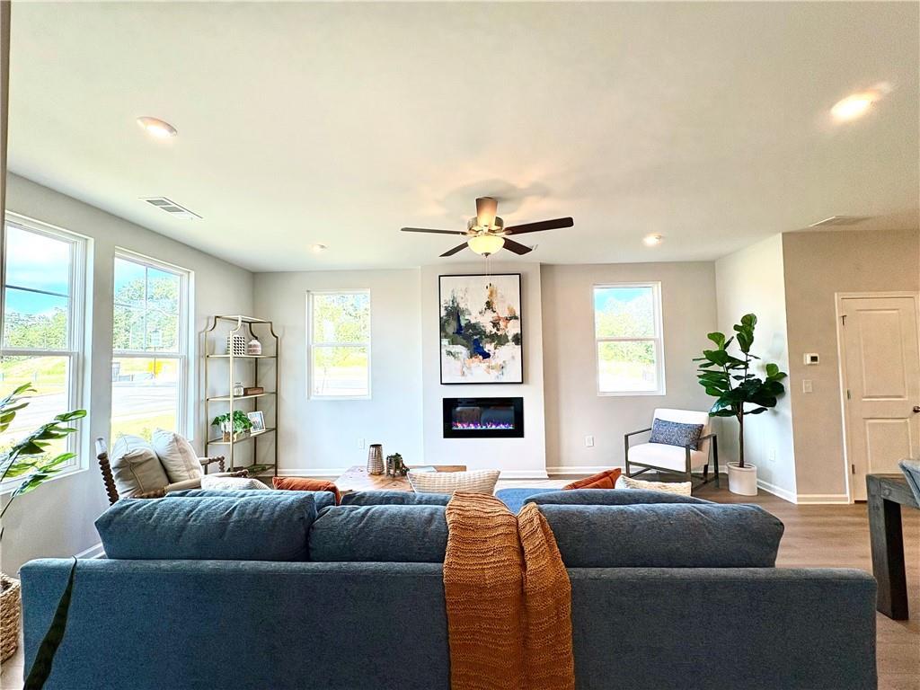 Cozy living room with blue sectional sofa, electric fireplace, abstract art, and large windows in Davidson Homes The Monroe A, Emerson, Georgia