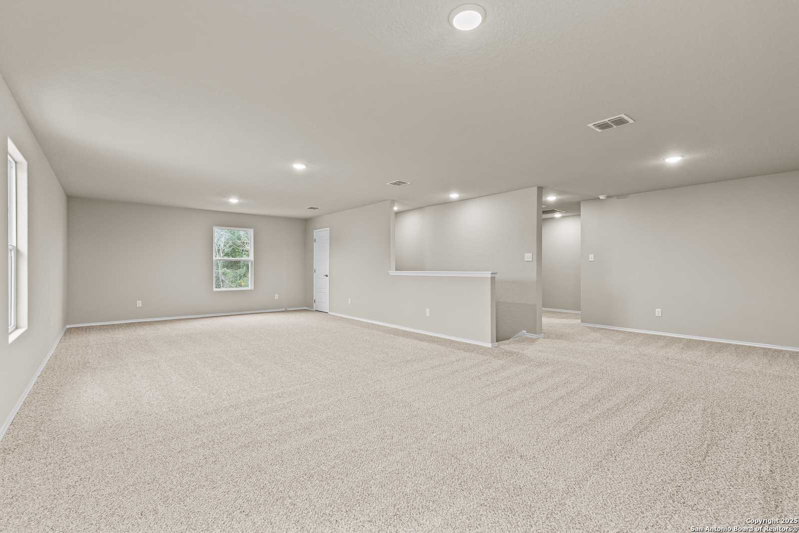 Spacious upstairs loft with beige carpet, light gray walls, recessed lights, large windows, and balcony overlook in Davidson Homes The Douglas F, San Antonio