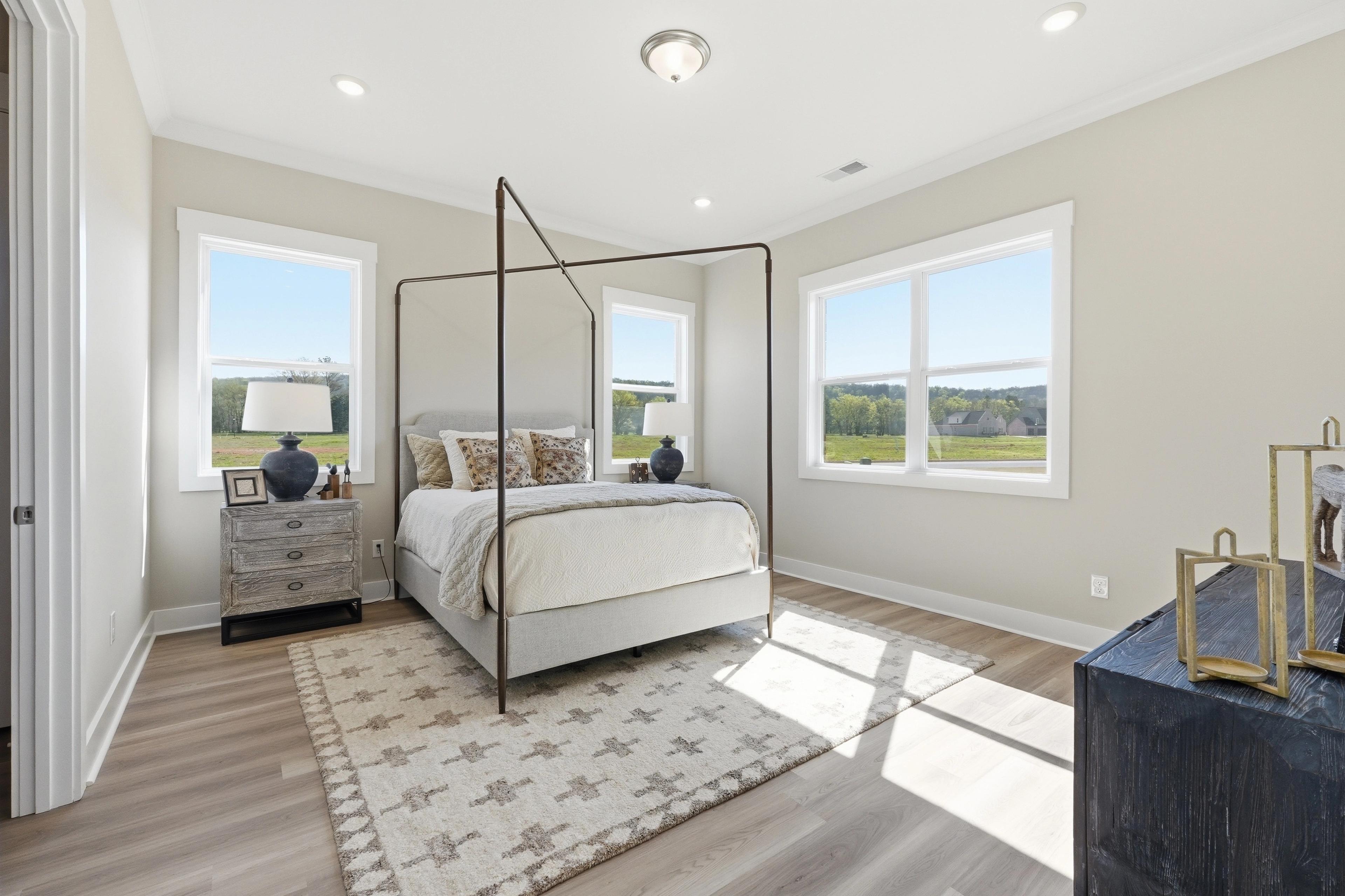 Spacious master bedroom interior at The Meadows at Hampton Cove in Owens Cross Roads AL featuring canopy bed, hardwood floors, and large windows
