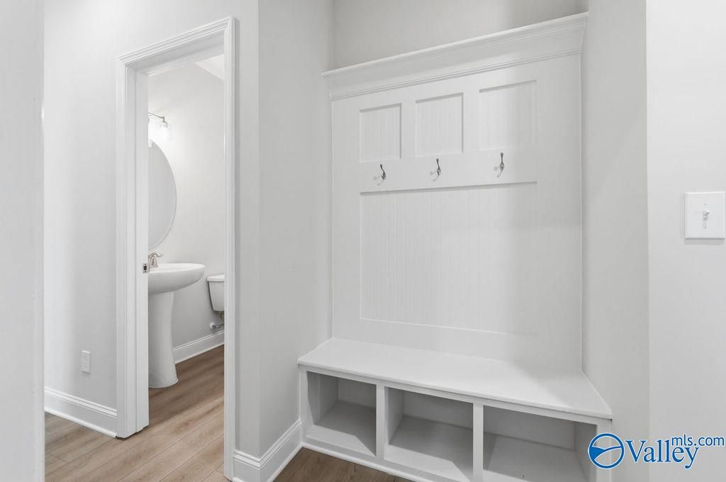 White mudroom with built-in bench, coat hooks, and adjacent powder room in Davidson Homes The Harrison, Hartselle Alabama