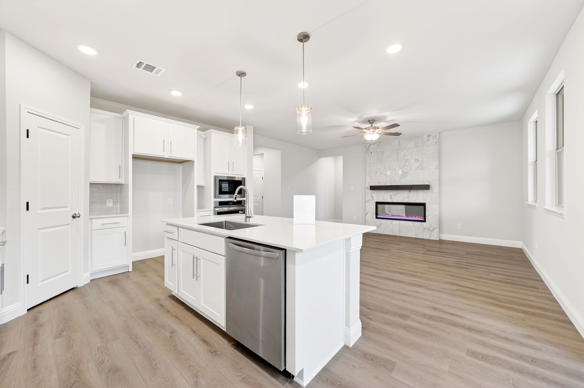 Open-concept kitchen and living area in The Redbud featuring a white island, modern appliances, and marble fireplace.