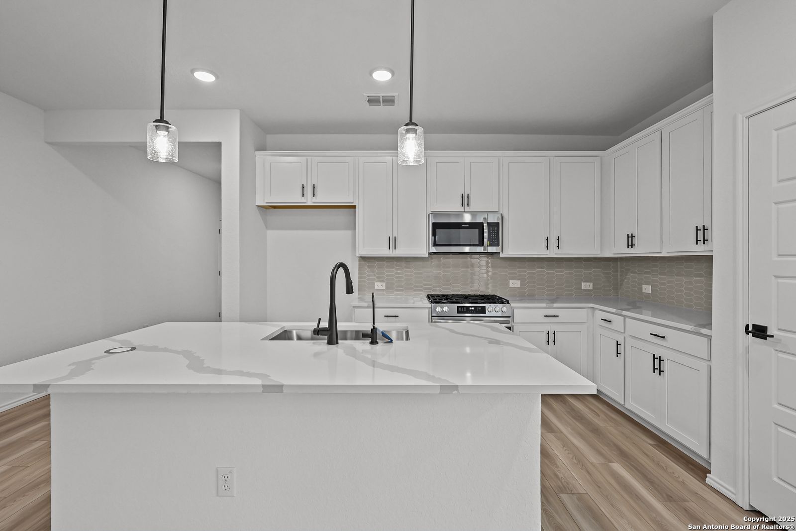 Modern white kitchen with quartz island, stainless appliances, and pendant lights in The Daphne J by Davidson Homes, Converse, TX