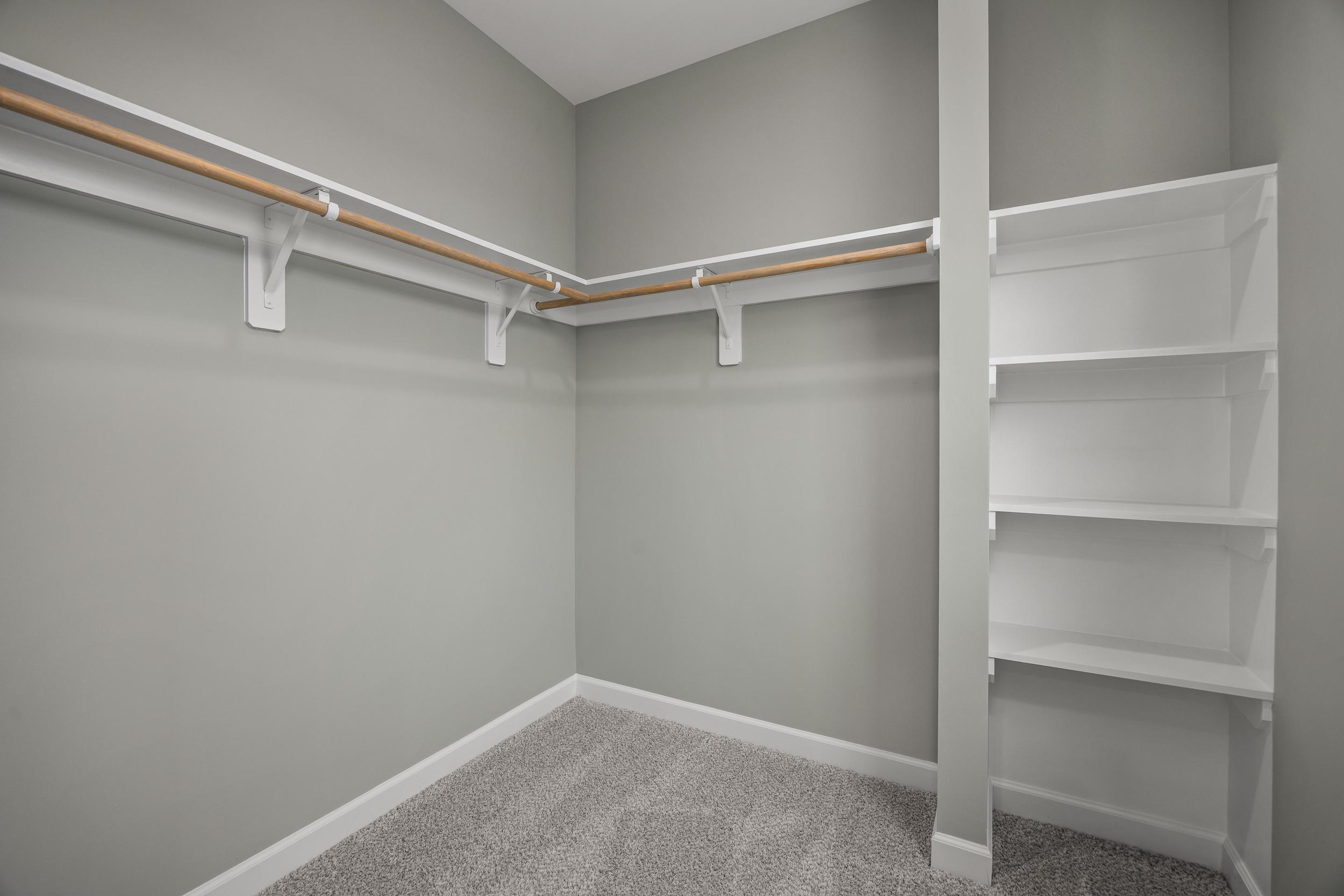 Spacious walk-in closet at Forestville Yard in Knightdale NC with gray walls, white shelving, wooden rods